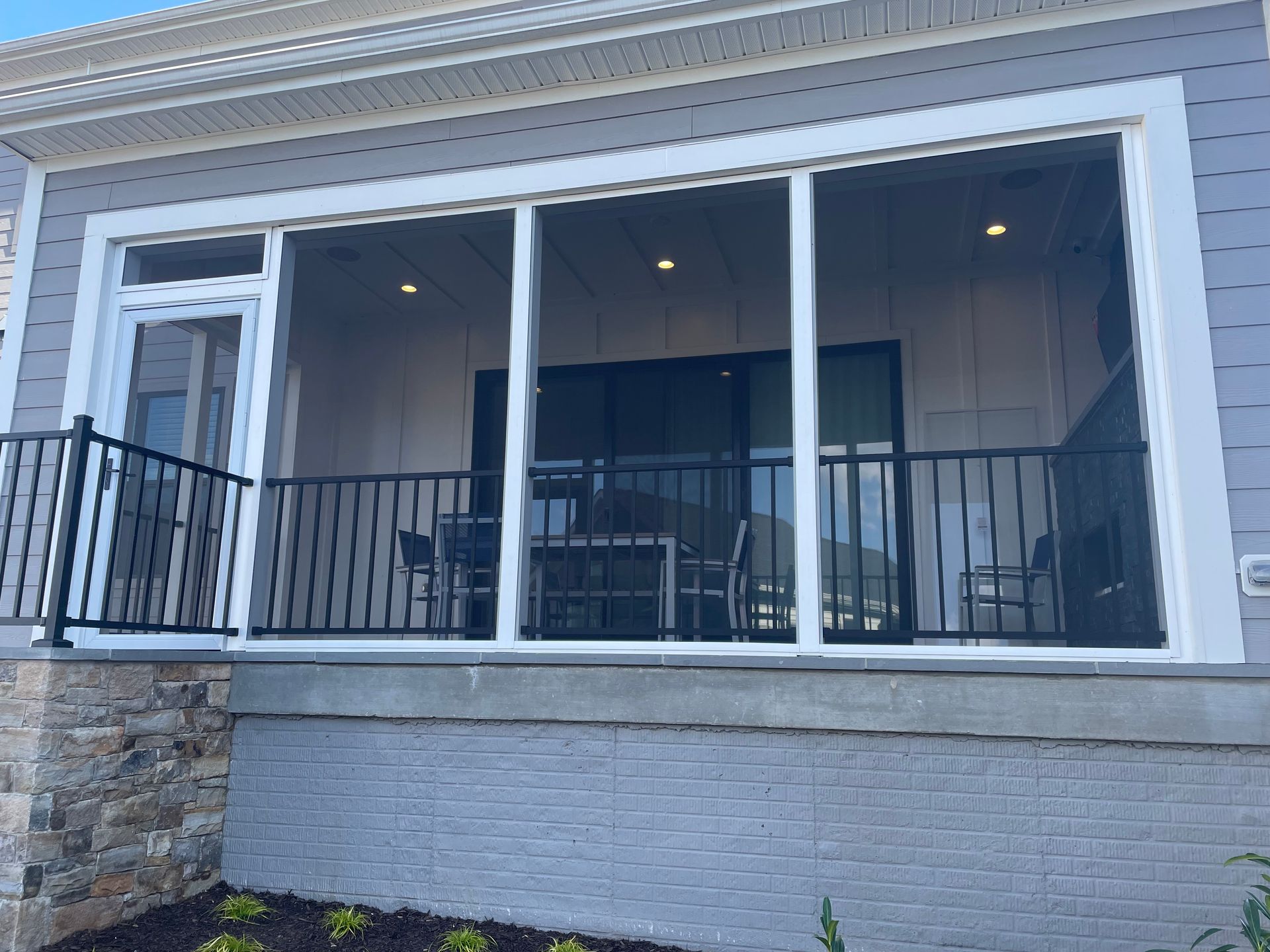 Screened porch with black railings, gray siding, and outdoor furniture.