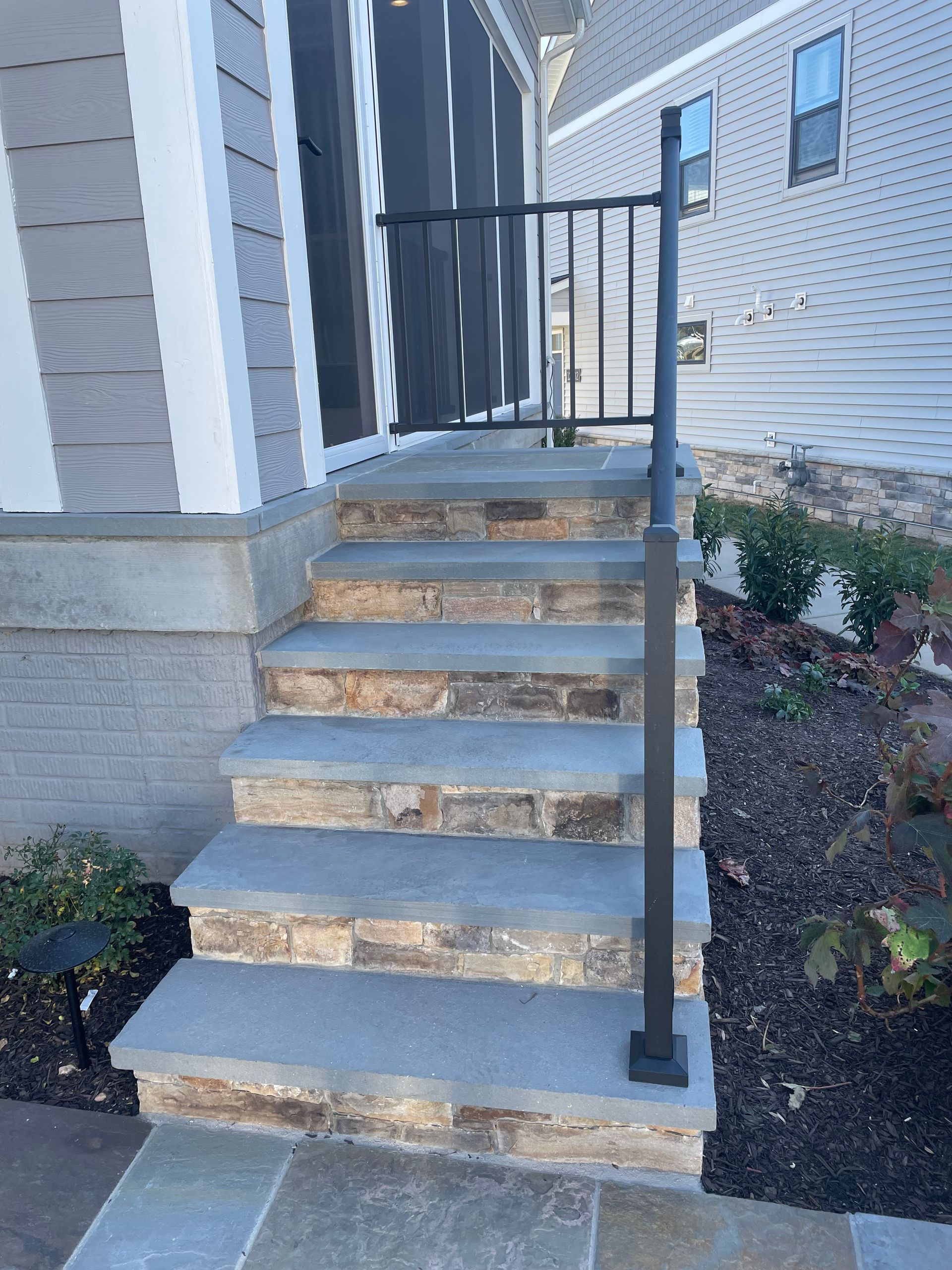 Stone steps leading to a front door with a black metal railing and gate.