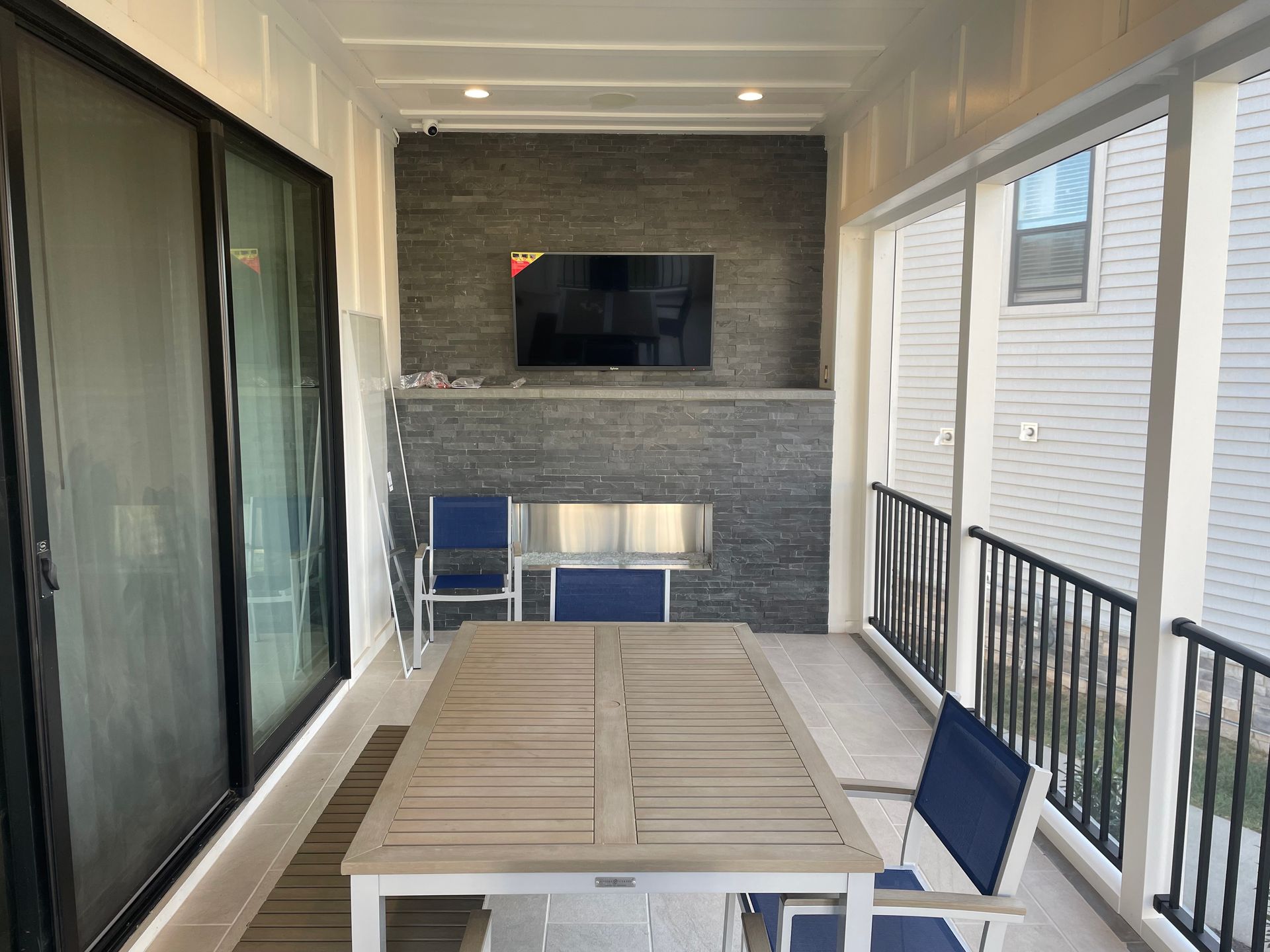Outdoor patio with a table, chairs, TV, and stone fireplace.