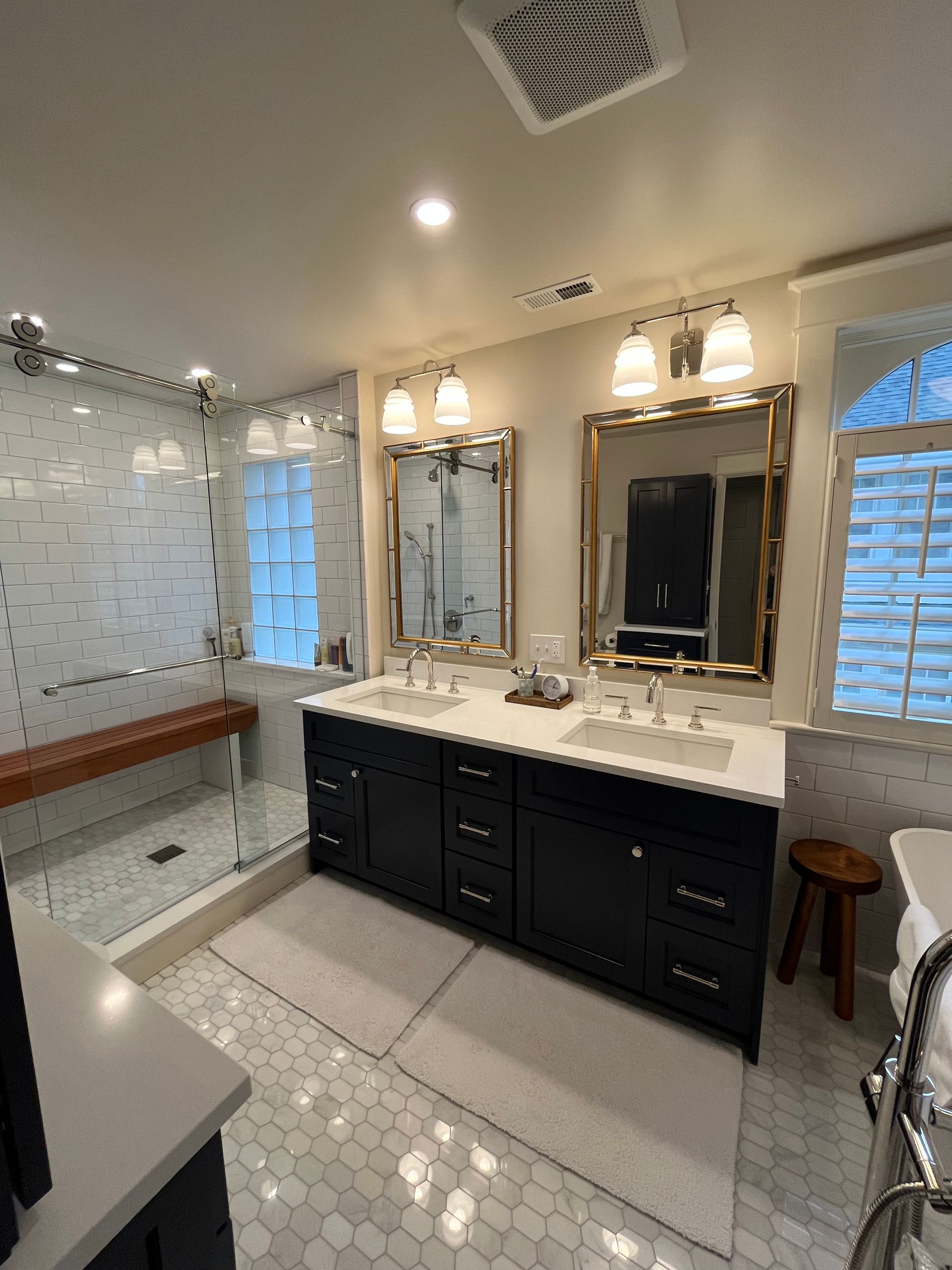 Bathroom with navy double vanity, white countertops, glass-enclosed shower, and hexagonal floor tiles.