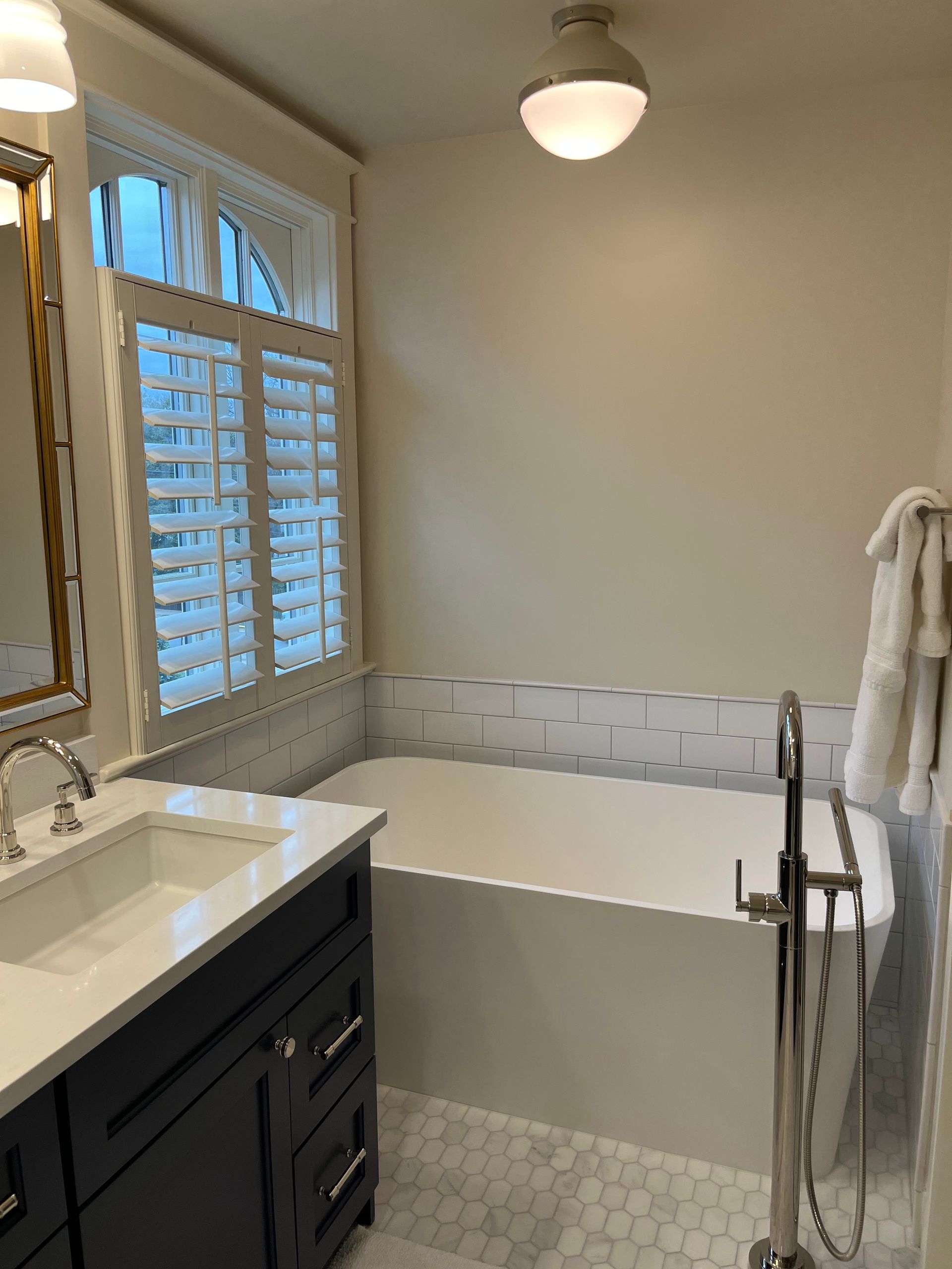 Bathroom with a white bathtub, vanity, and window with shutters.