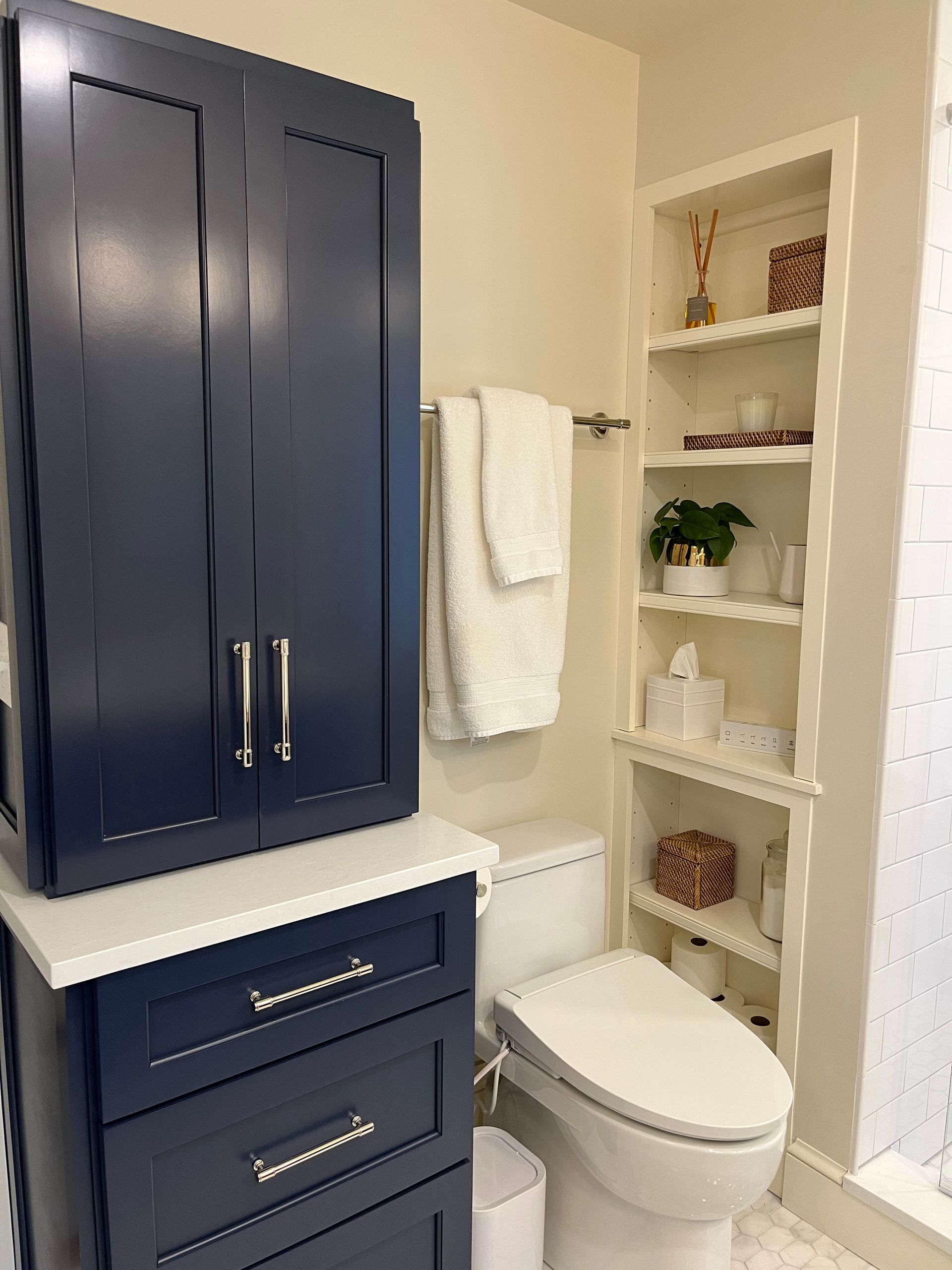 Navy blue bathroom cabinet with white countertop, towel bar, toilet, and built-in shelving.