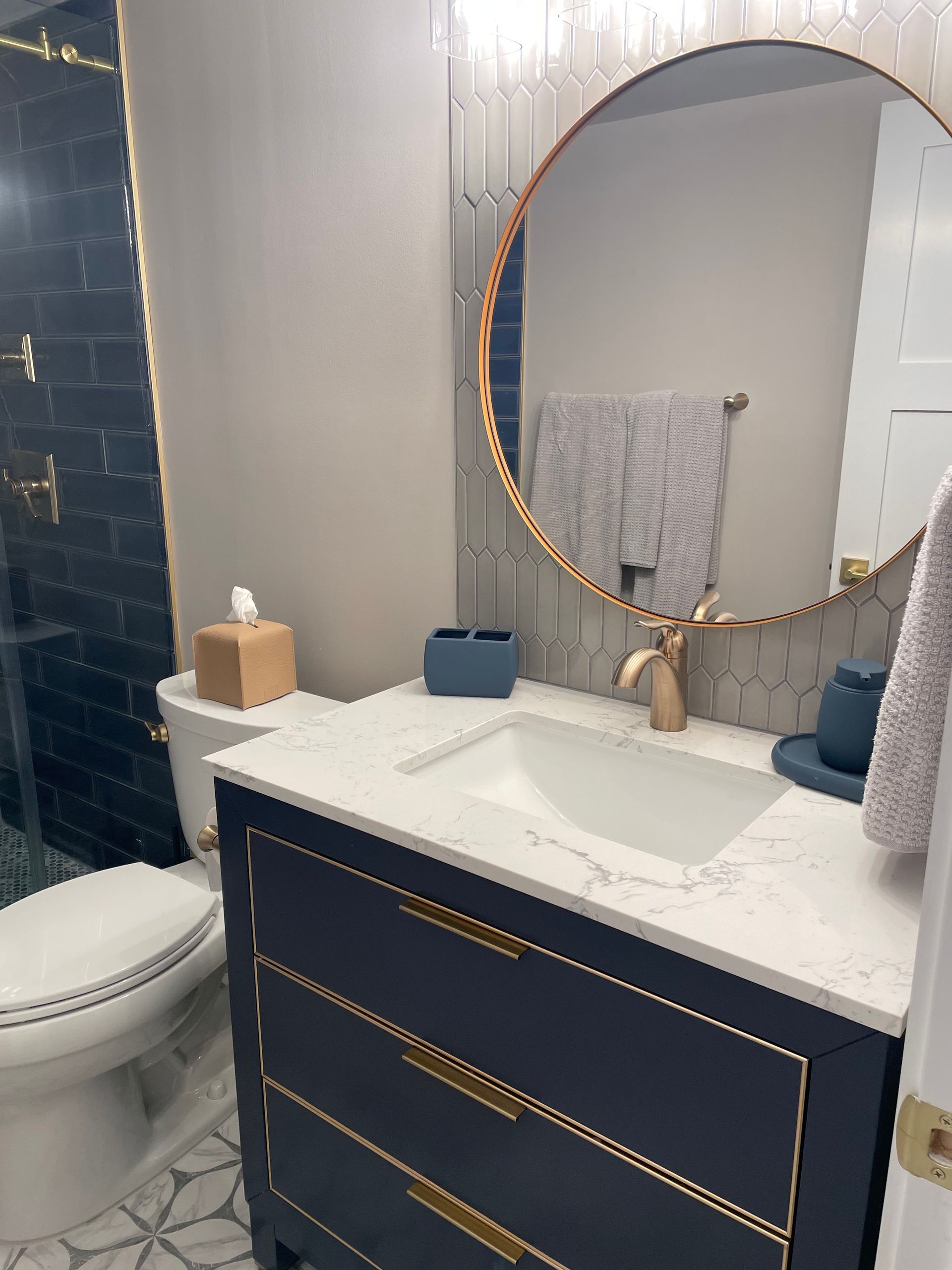 Modern bathroom with a navy vanity, gold accents, and a round mirror.