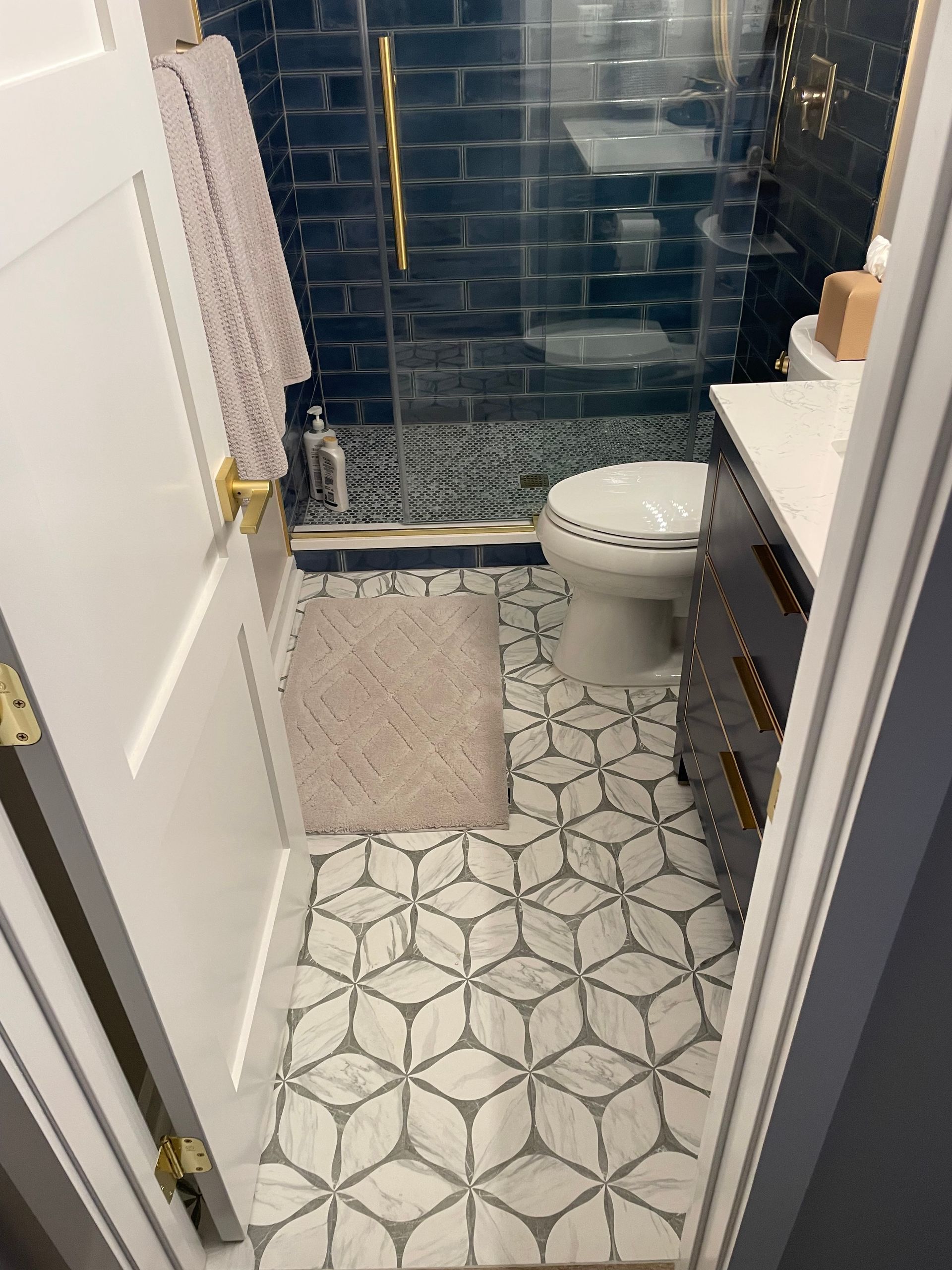Bathroom with patterned floor tiles, dark blue shower tiles, and a white toilet.
