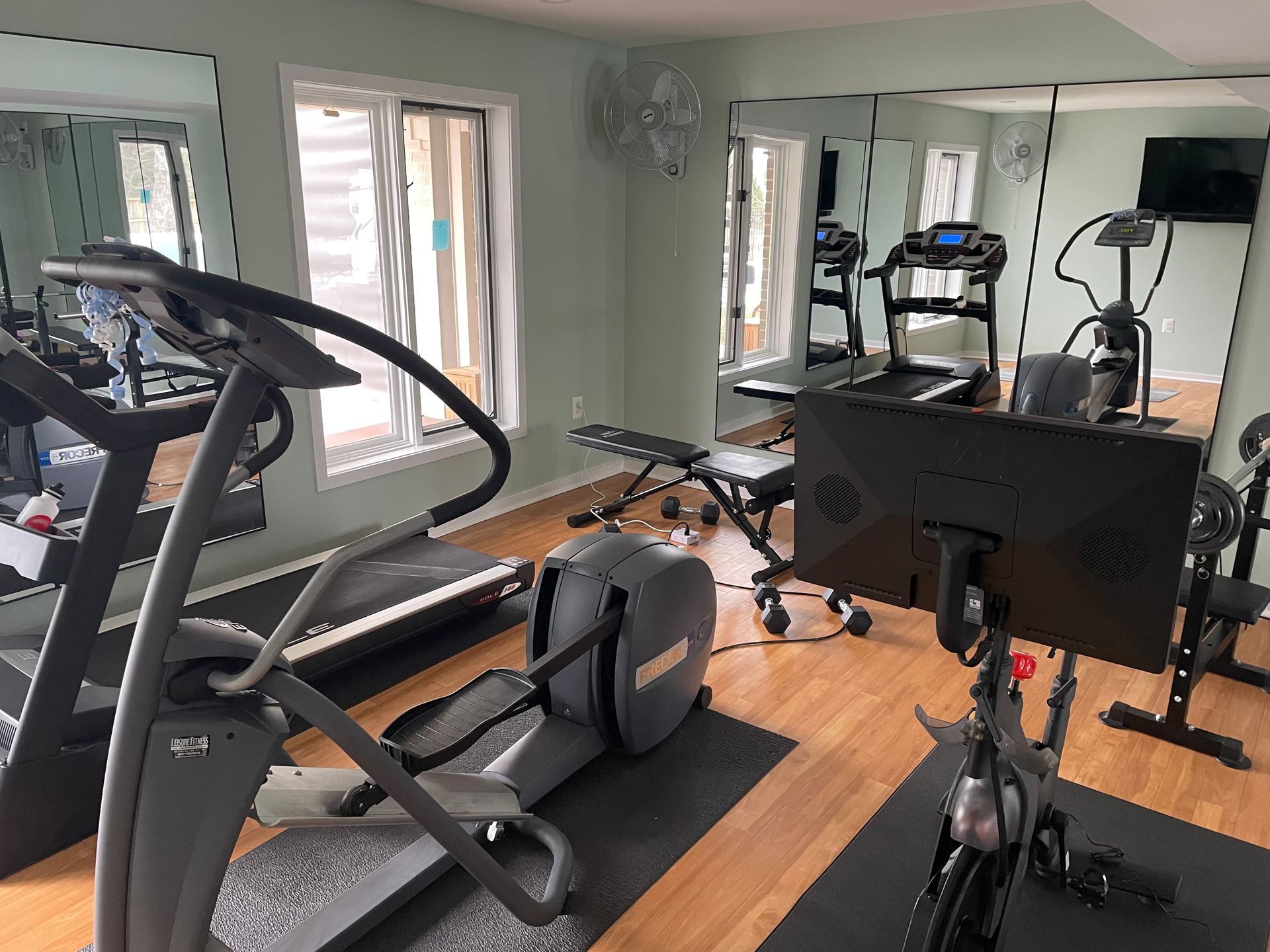 Gym with treadmills, elliptical, exercise bike, weight bench, and large mirrors on the walls.