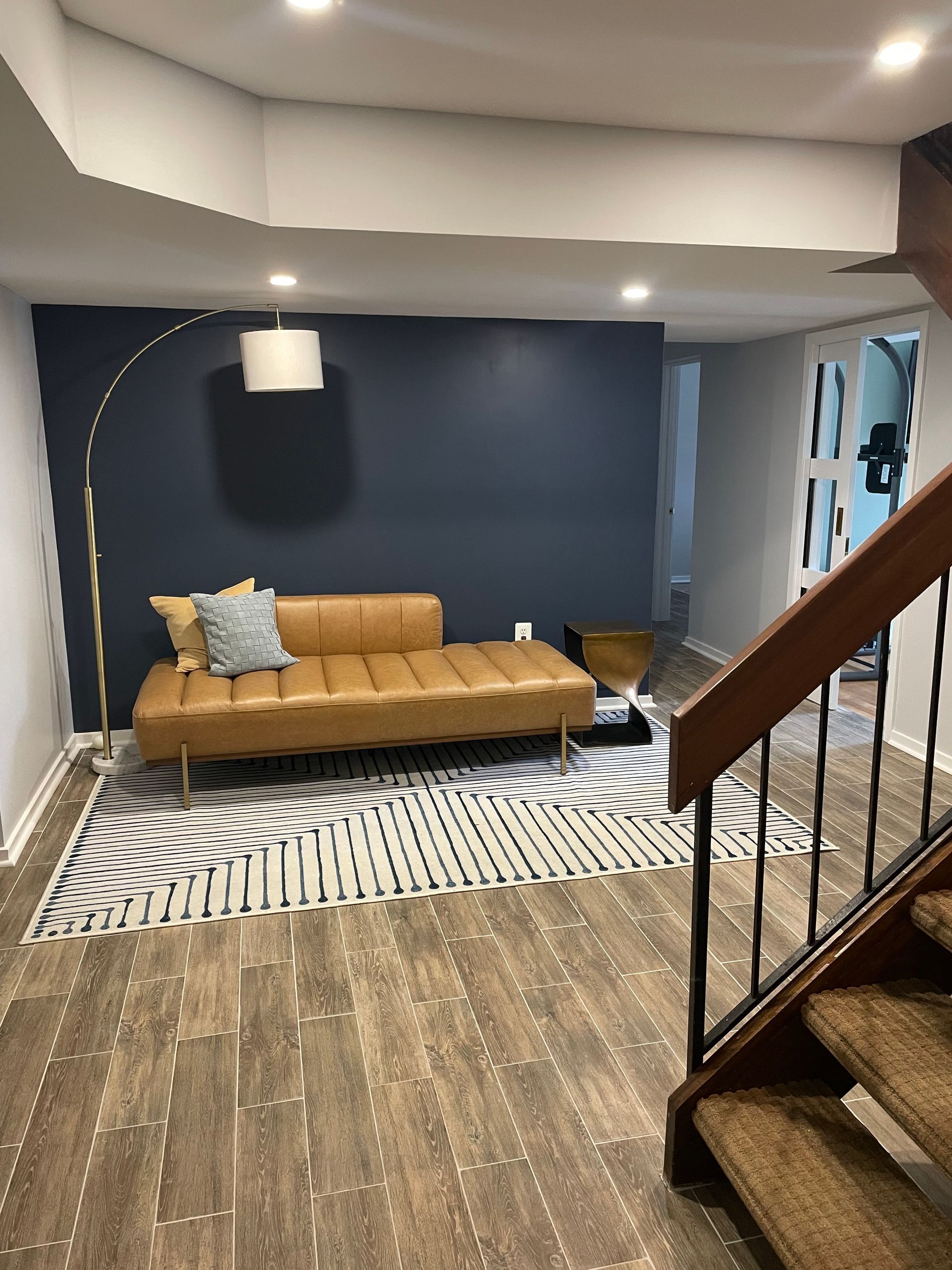 Living room with brown leather sofa, navy wall, patterned rug, and stairs.