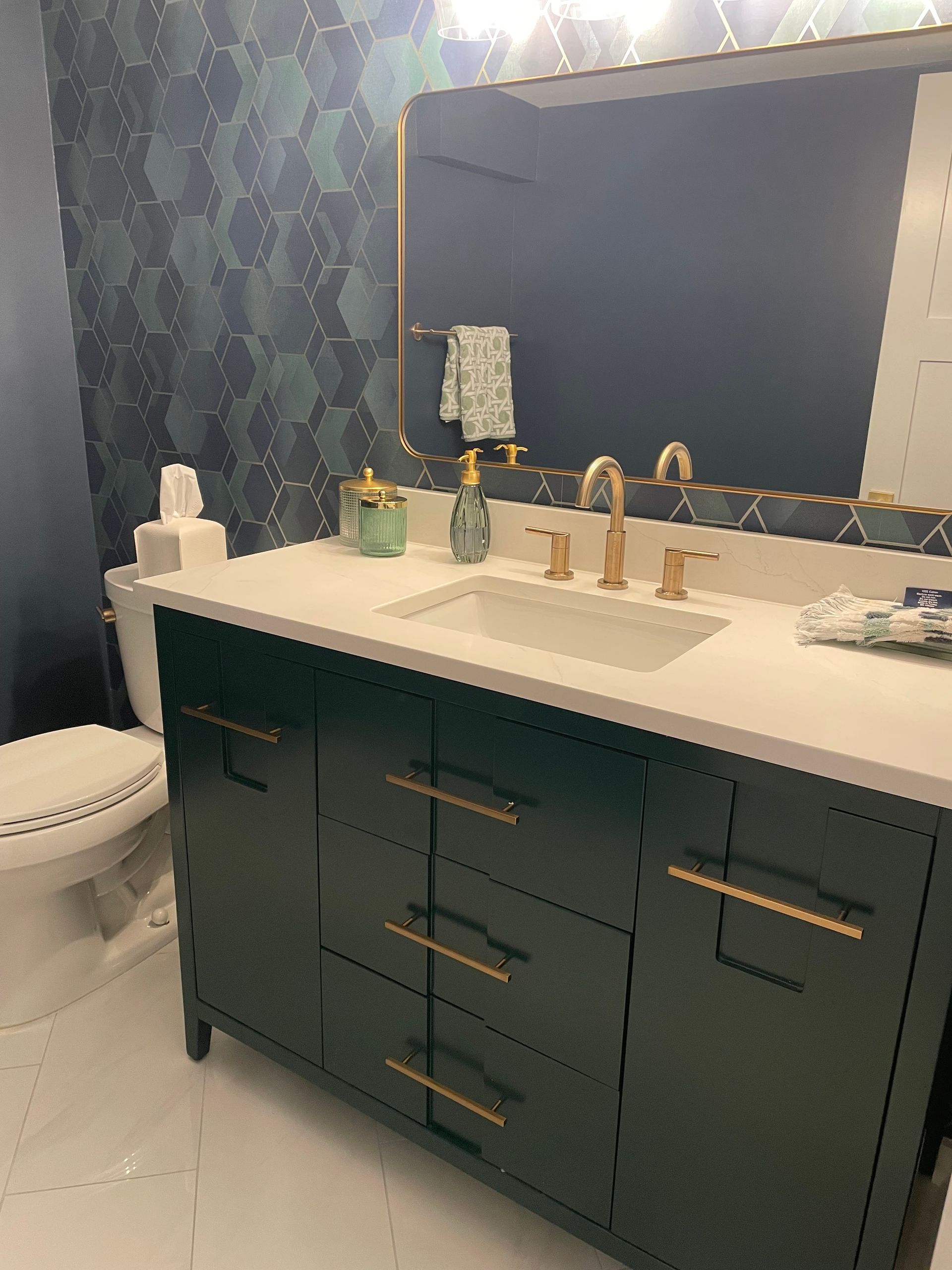 Dark green bathroom vanity with gold hardware, white countertop, sink, and hexagonal tile backsplash.