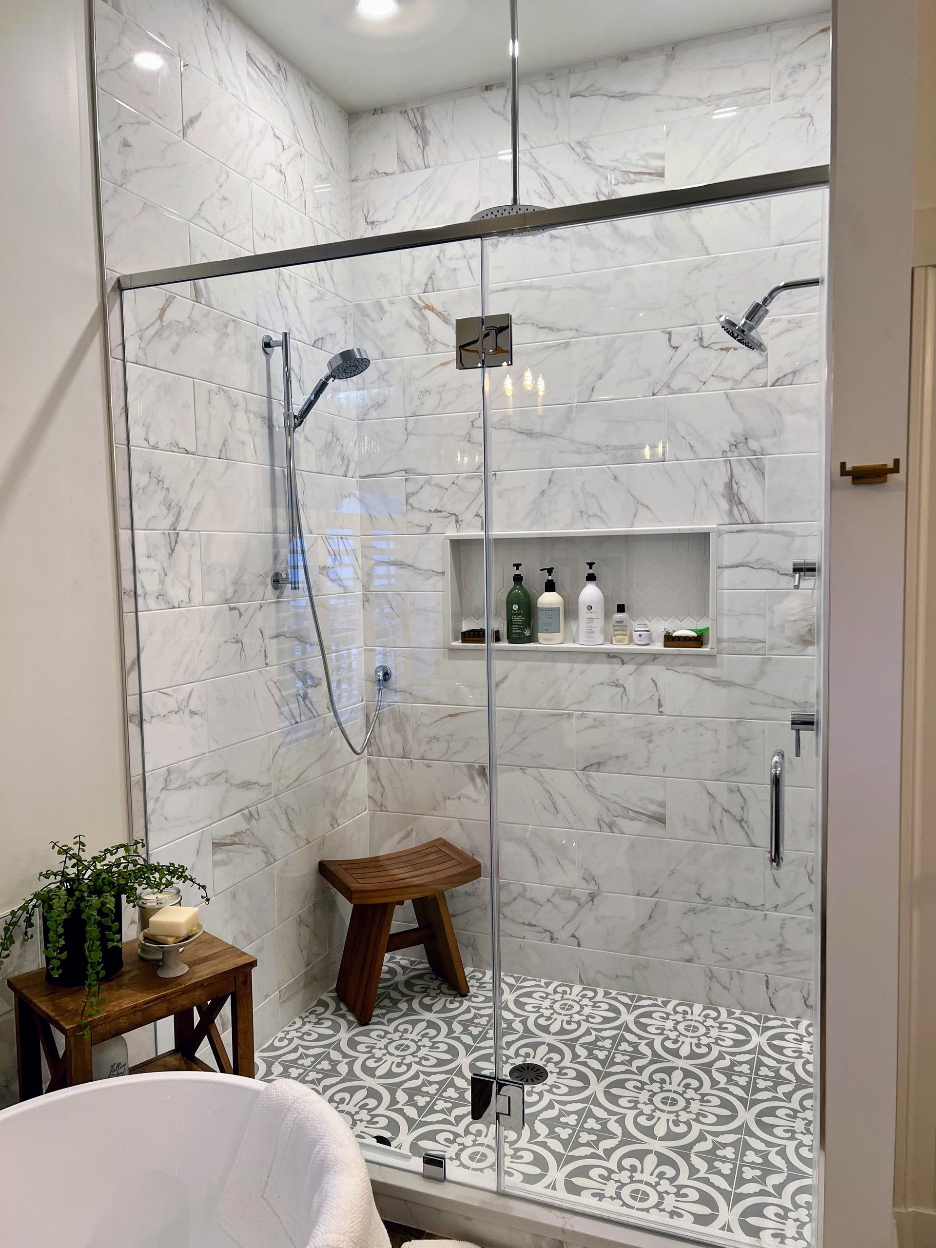 Bathroom with marble tile walls, glass shower door, and wooden stool.