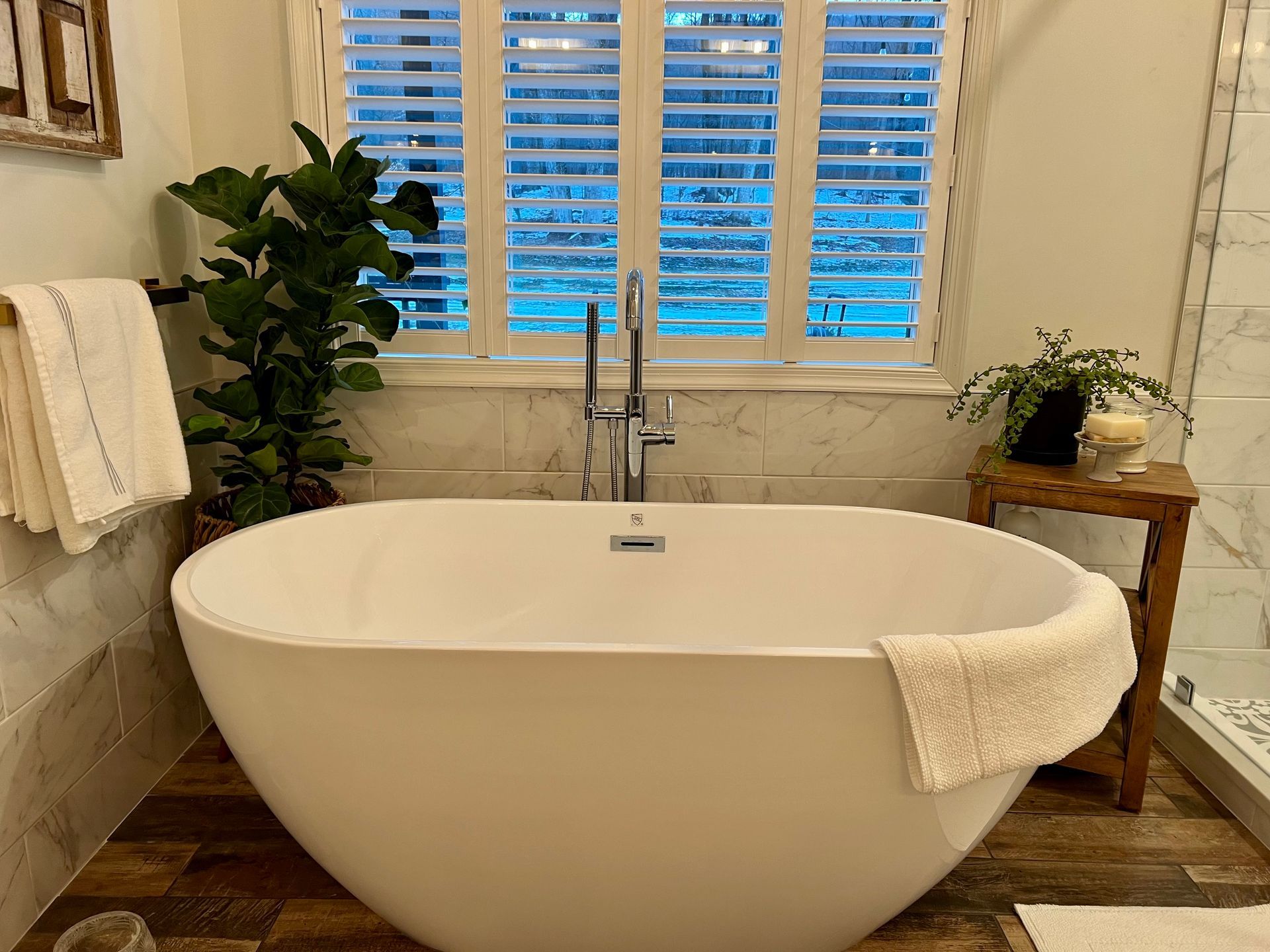 White oval bathtub in a bathroom, with a window and plants.