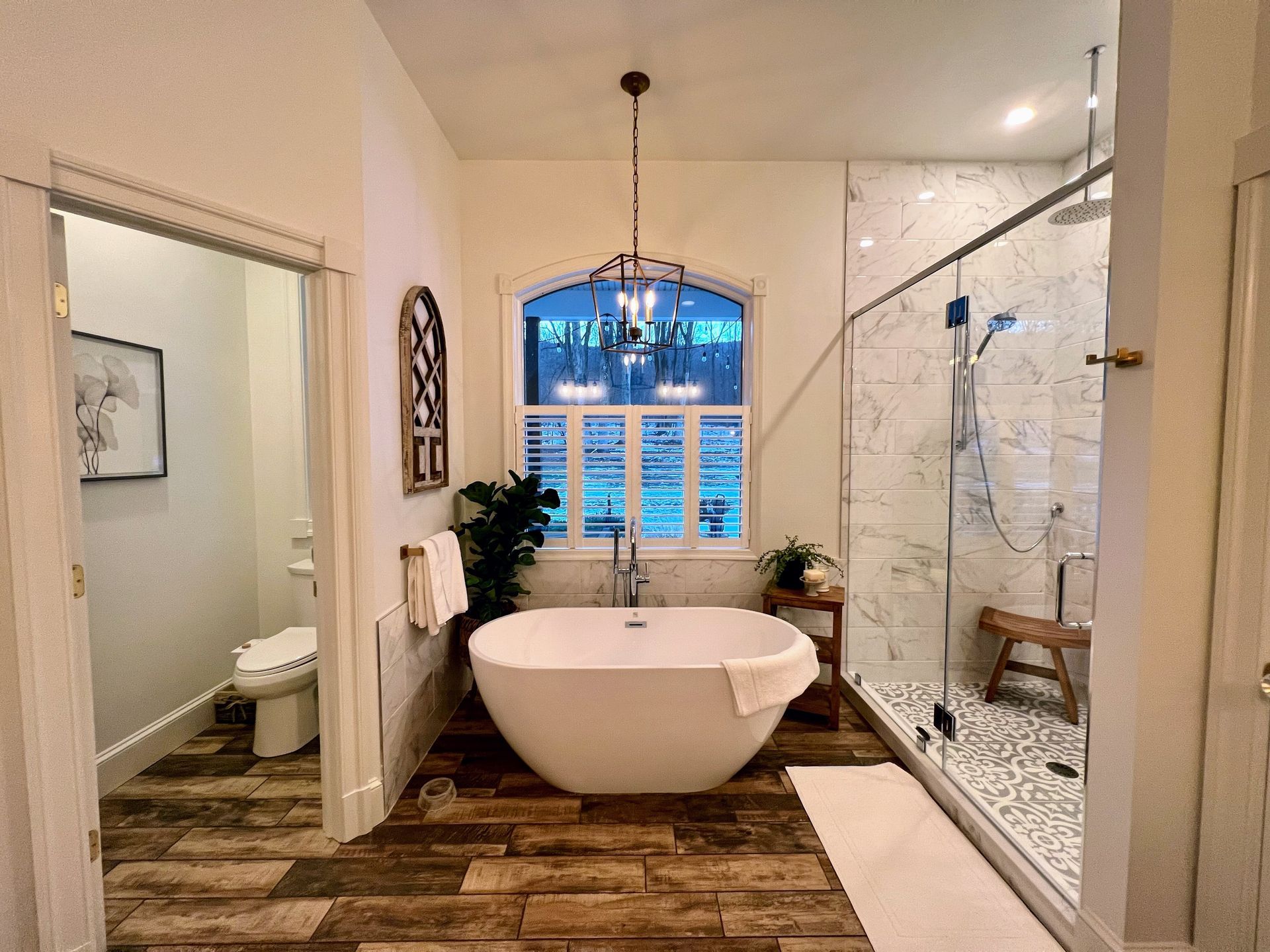 Bathroom with freestanding tub, walk-in shower, and closed toilet room. Features wood-look flooring and white walls.