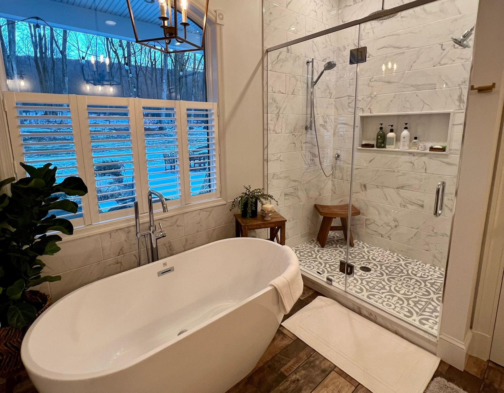 Modern bathroom with white tub, walk-in shower, window with shutters, and wooden accents.