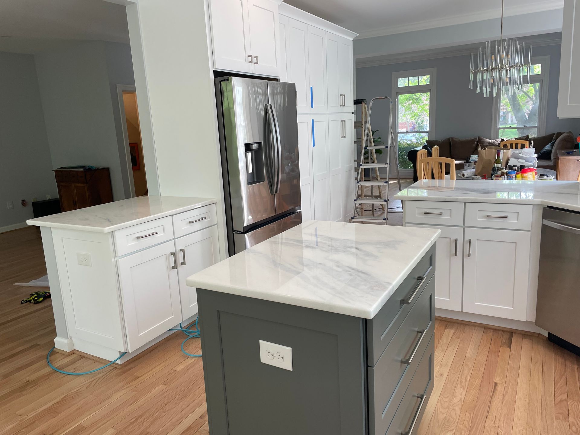 Kitchen with white cabinets, gray island, stainless steel refrigerator, and hardwood floors.