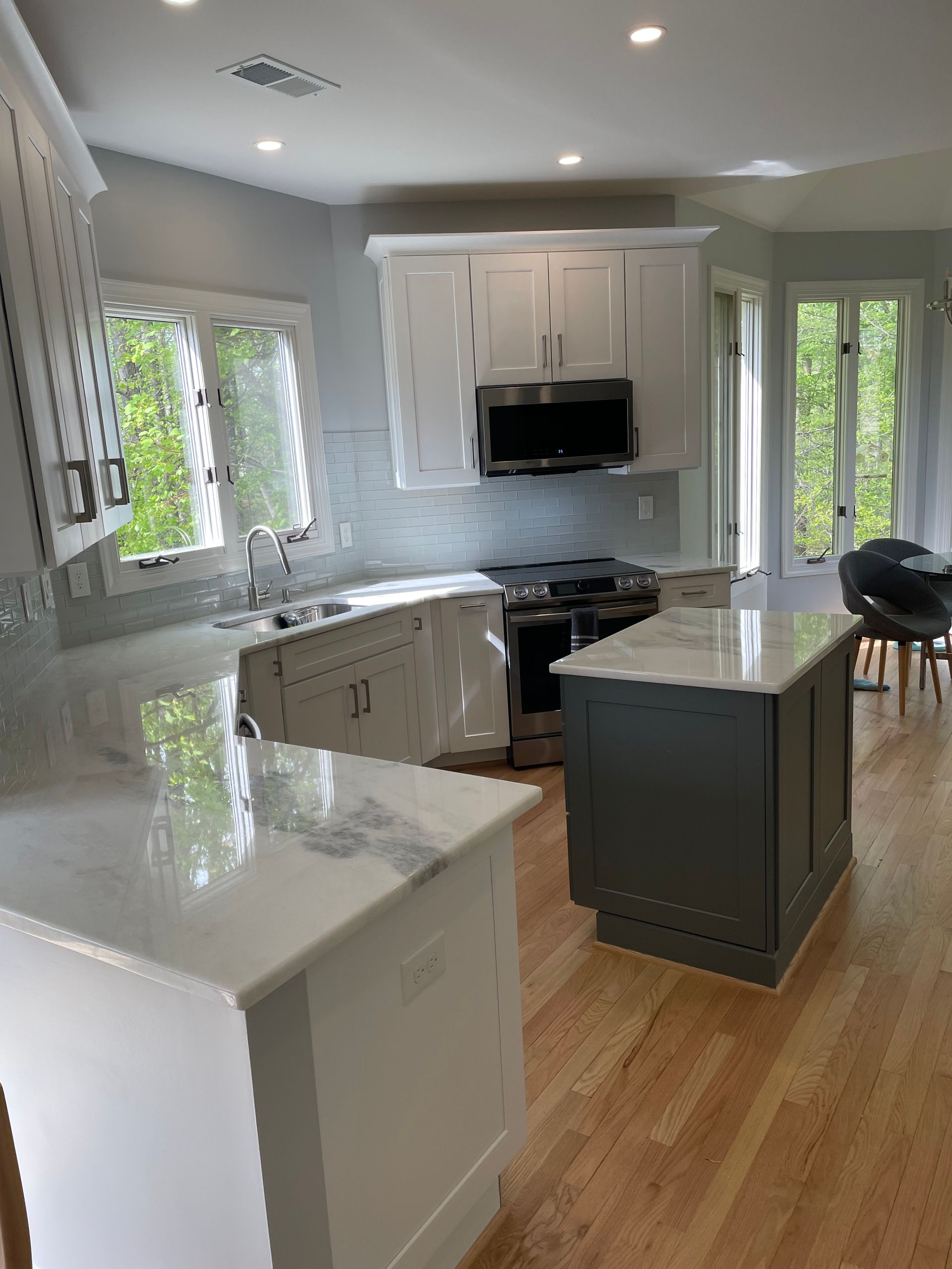 Modern kitchen with white countertops and cabinets, gray island, stainless steel appliances, and wooden floors.