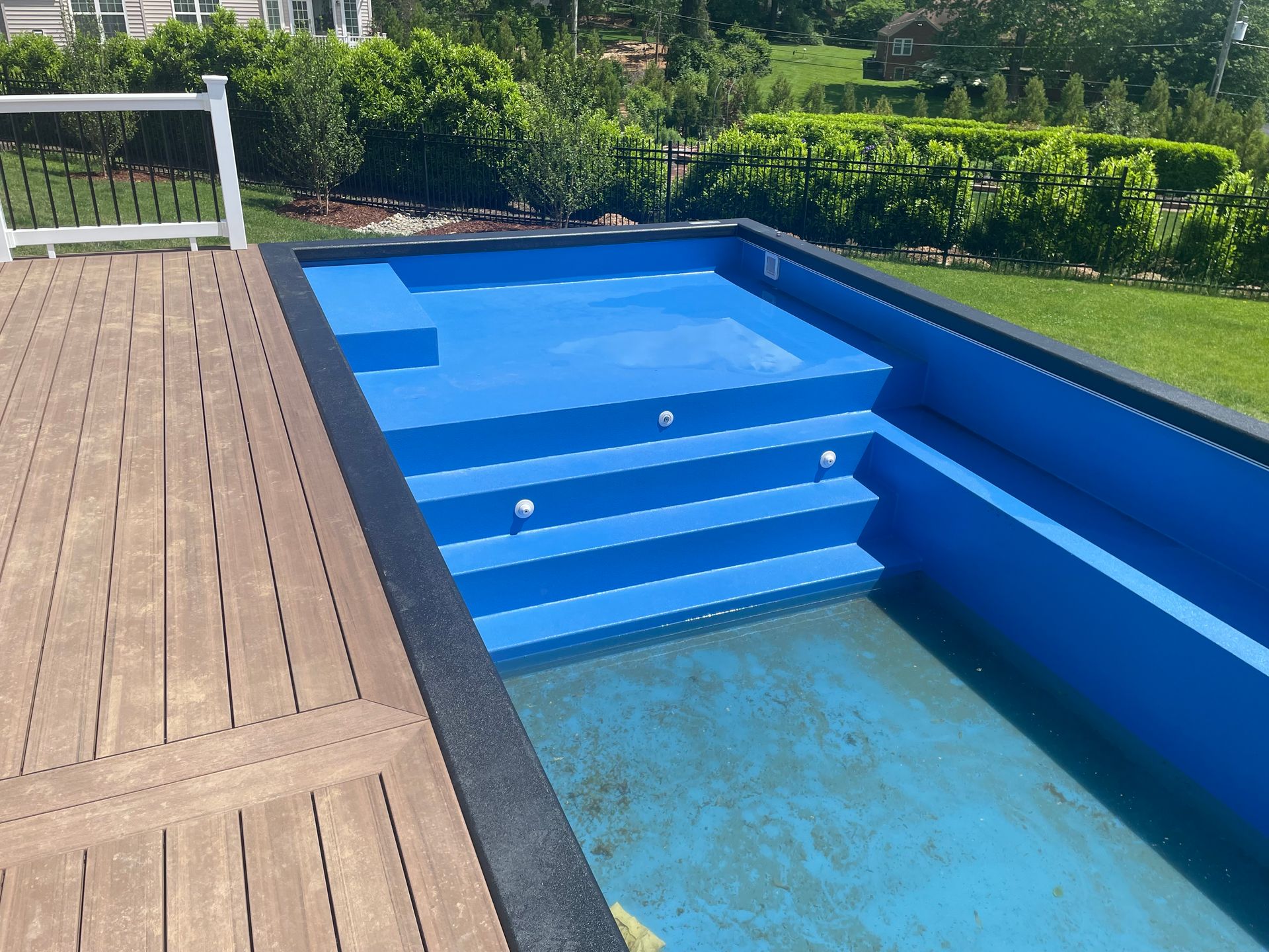 Blue rectangular pool with steps, next to a wooden deck, outdoors.