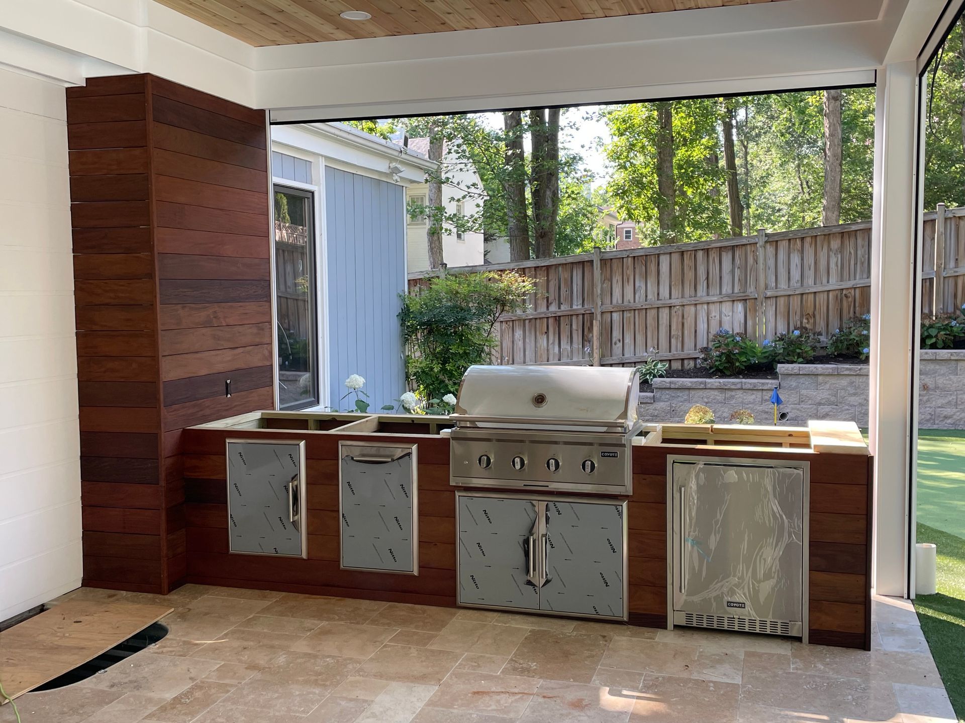 Outdoor kitchen with brown wood cabinets, stainless steel appliances, and beige tile floor.