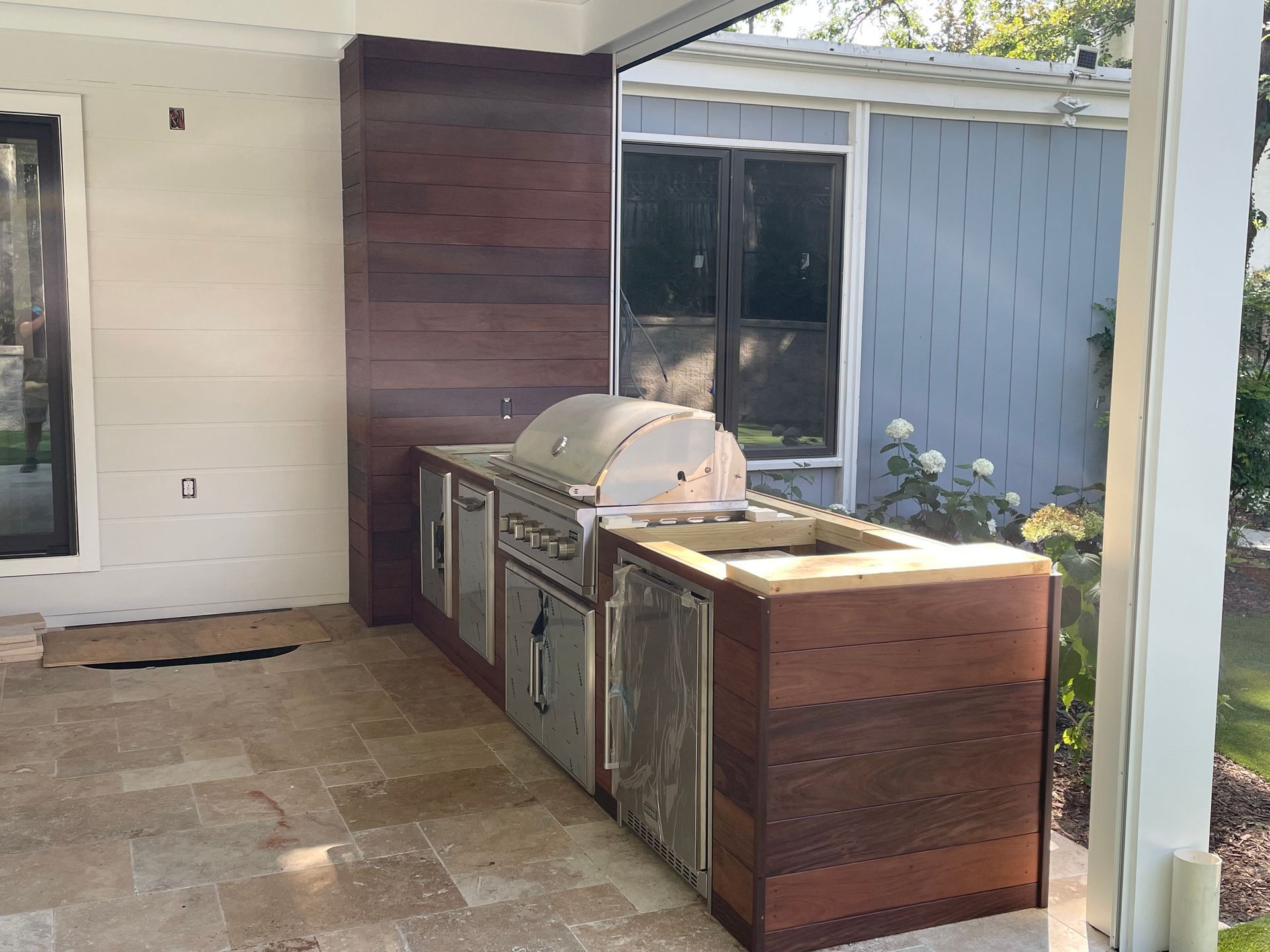 Outdoor kitchen with wooden cabinets and stainless steel appliances; sits on stone patio.