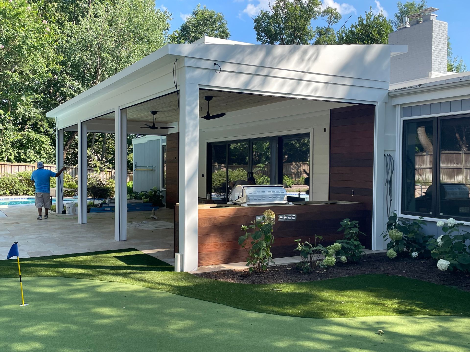 Outdoor patio with a white pergola, grill, and view of a pool and green lawn.