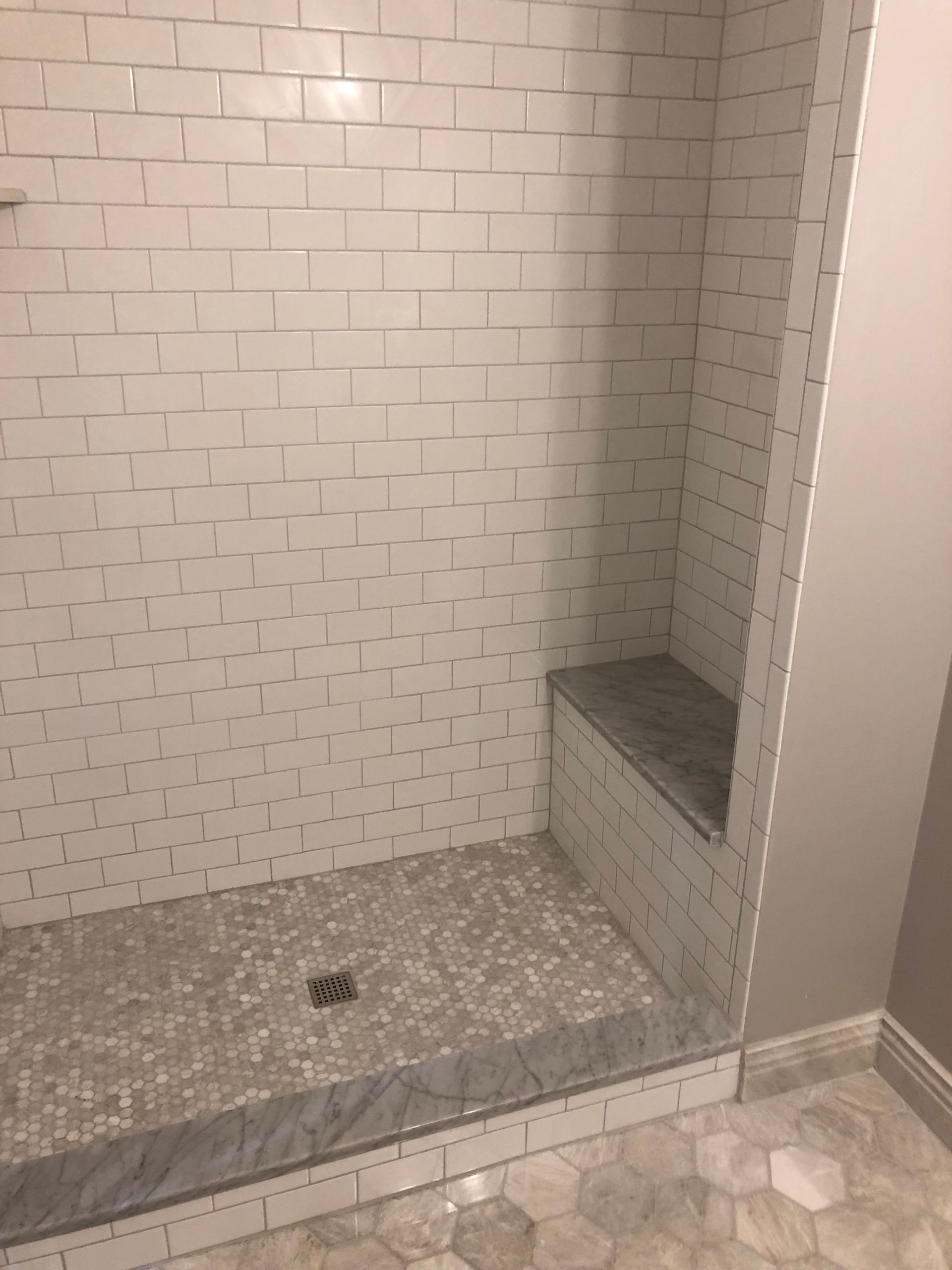 Shower with white subway tile walls, gray bench, and hex tile floor.