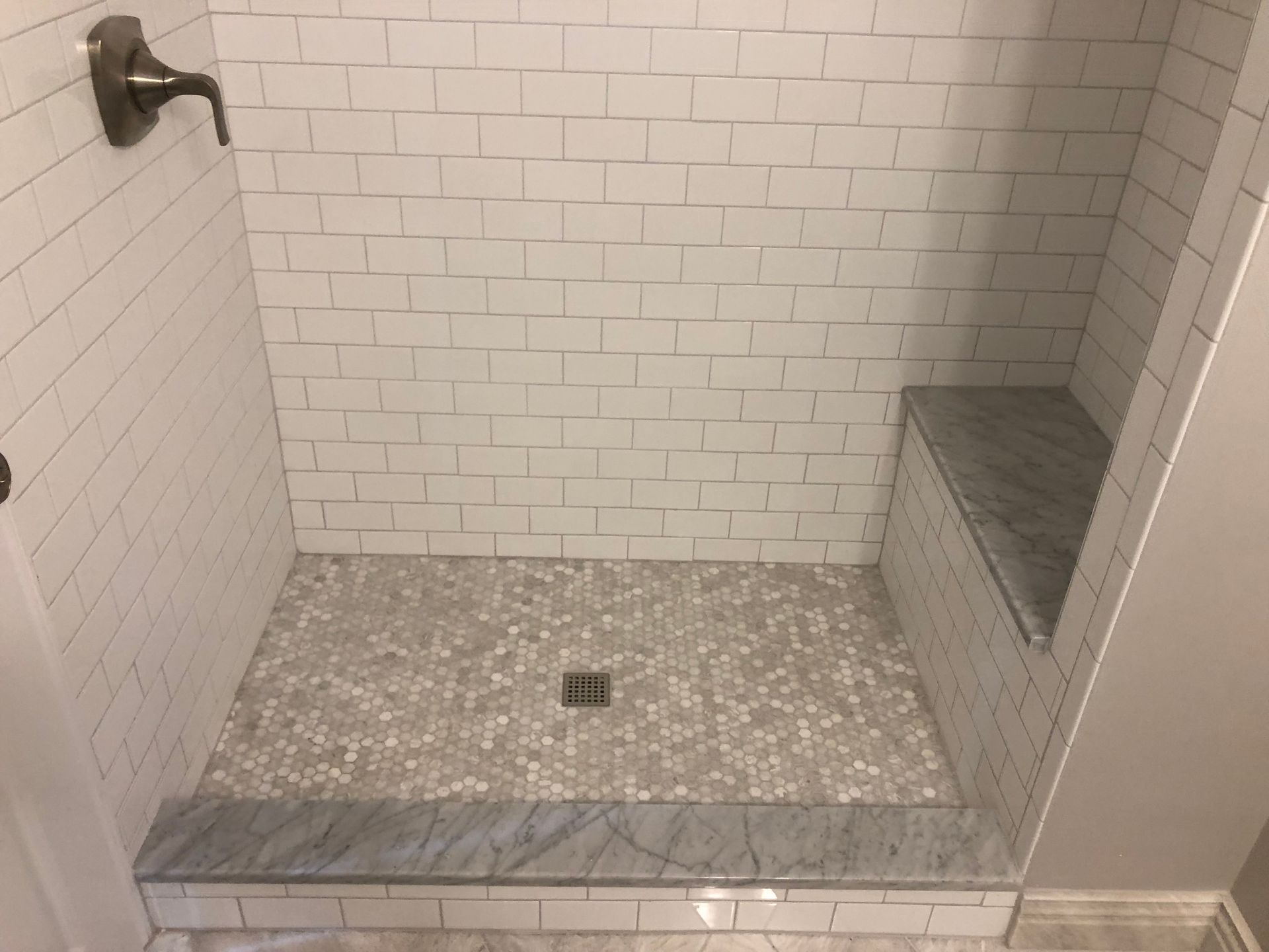 Shower with white subway tile walls, pebble tile floor, and a marble bench.