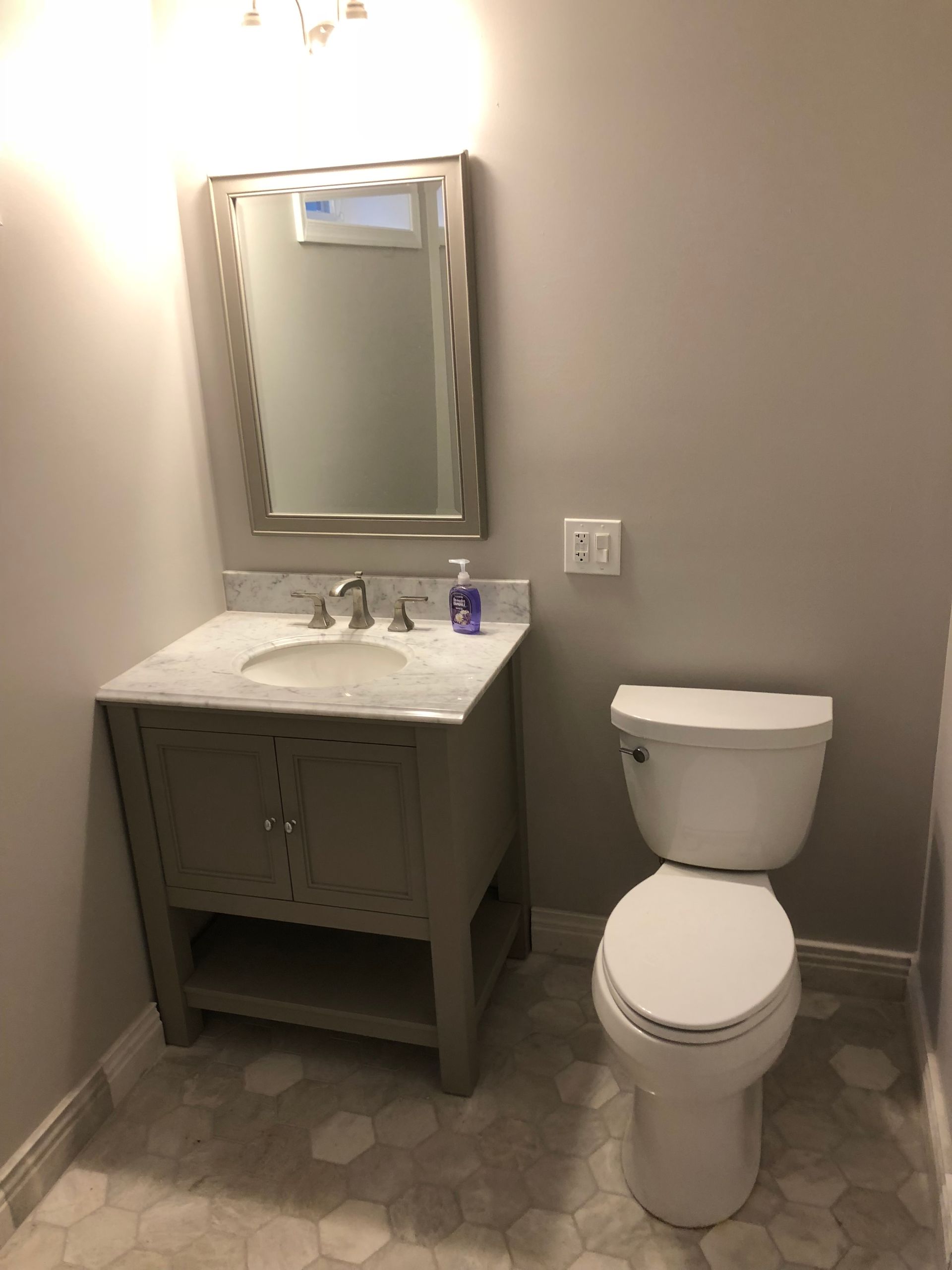 Gray bathroom with vanity, mirror, toilet, and hexagonal floor tiles.