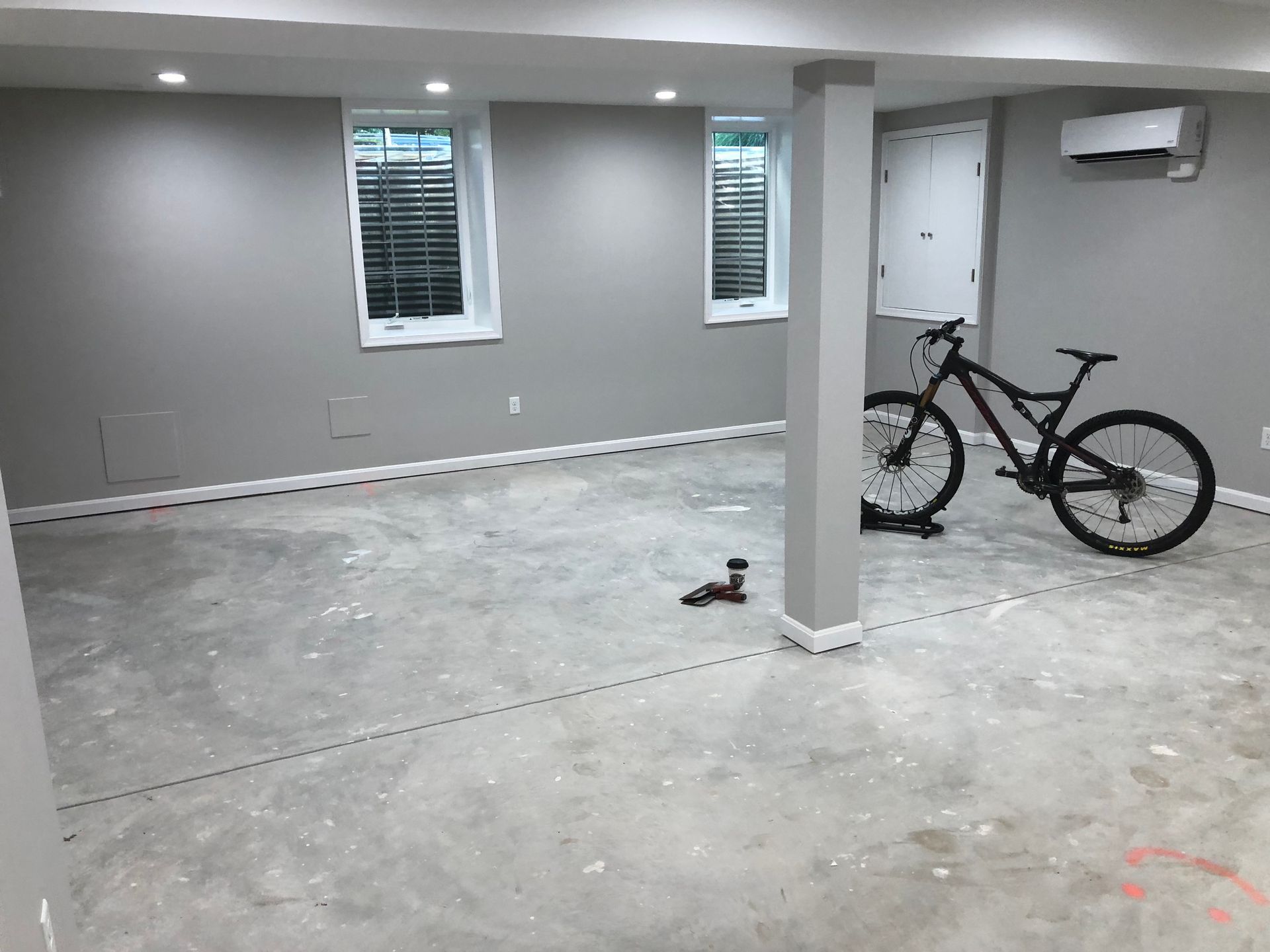 Basement interior with gray walls, two small windows, a support beam, a bicycle, and concrete floor.