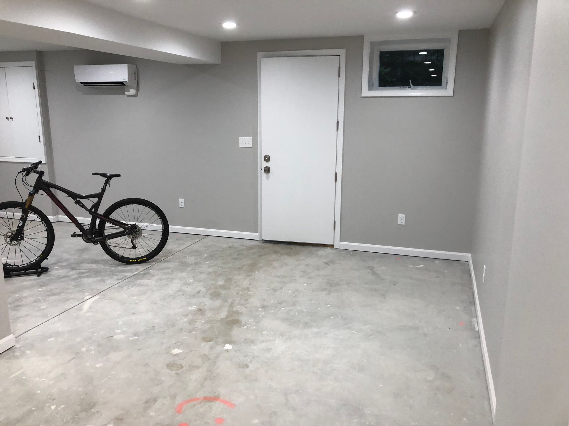 A mostly empty room with a mountain bike. Gray walls, white door and trim, concrete floor.