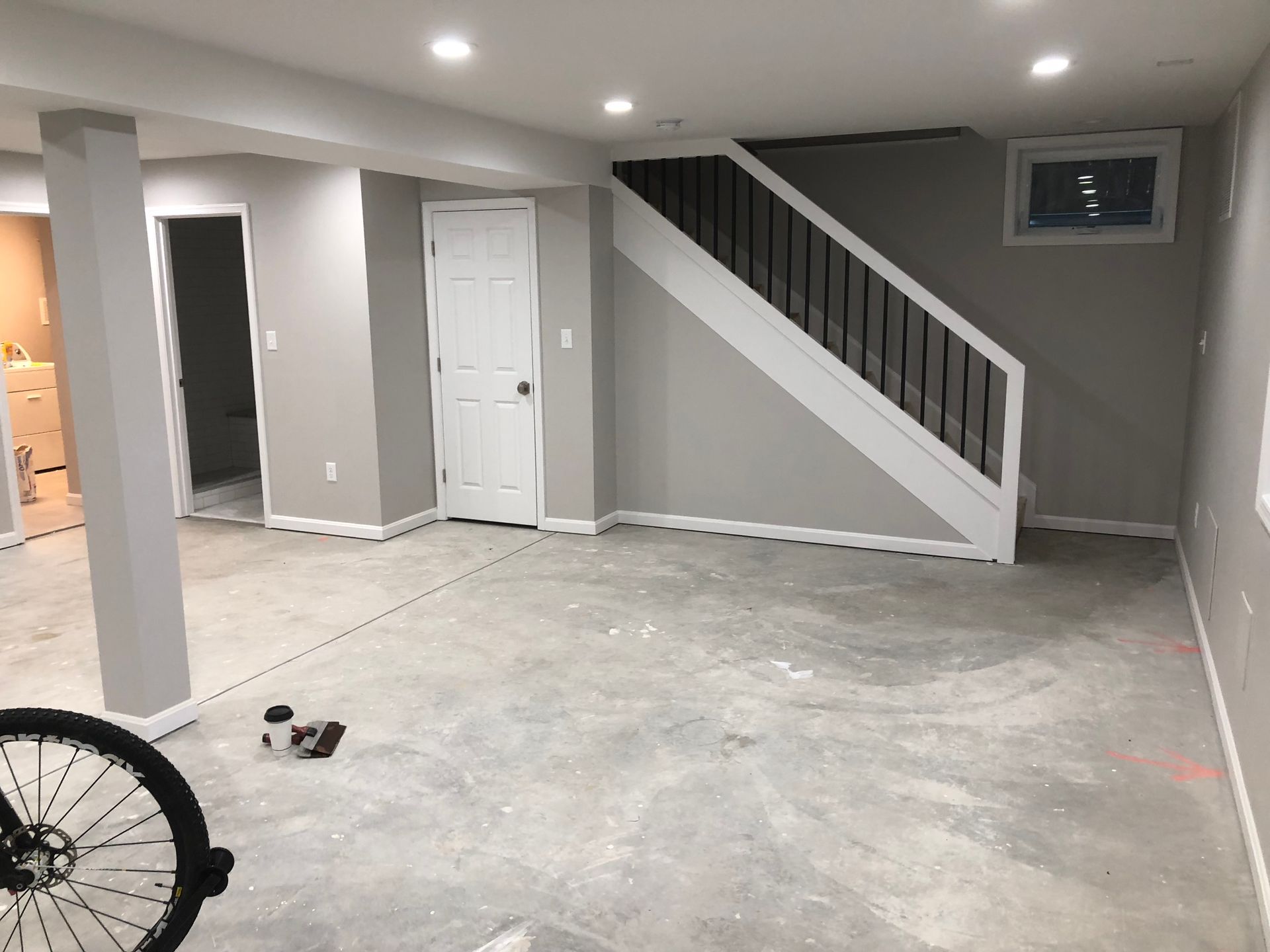 Finished basement interior with gray walls, white trim, stairs, and concrete floor.
