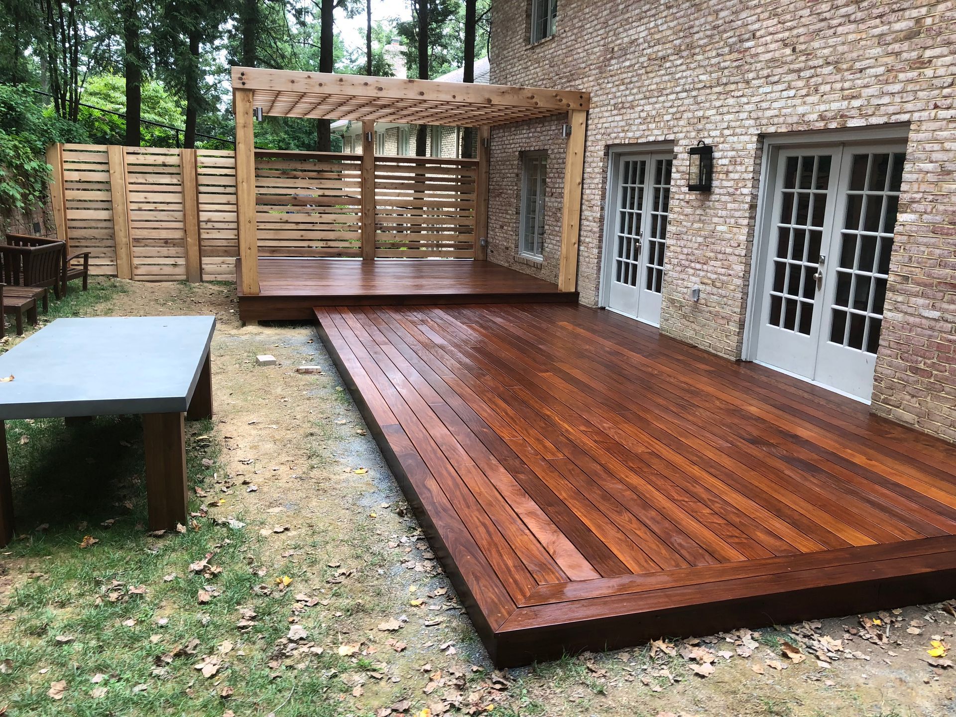 Wooden deck with pergola next to brick house; outdoor dining table and wooden fence visible.
