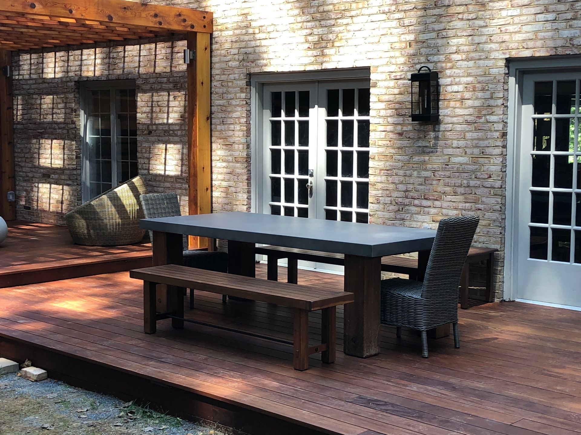 Outdoor dining set on a wooden deck in front of a brick building with French doors.