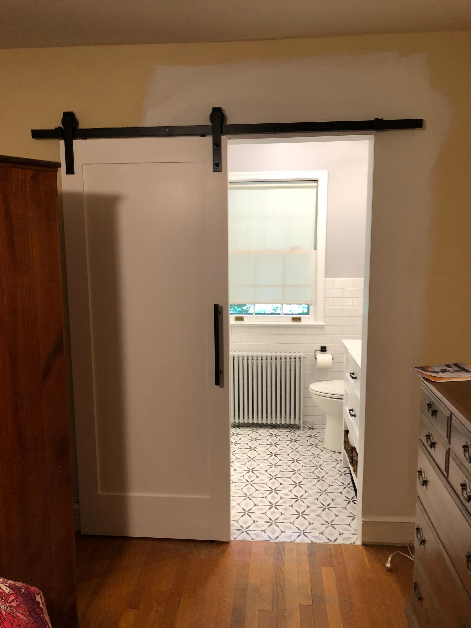 White sliding barn door, black hardware, open to a bathroom with a window and patterned floor.