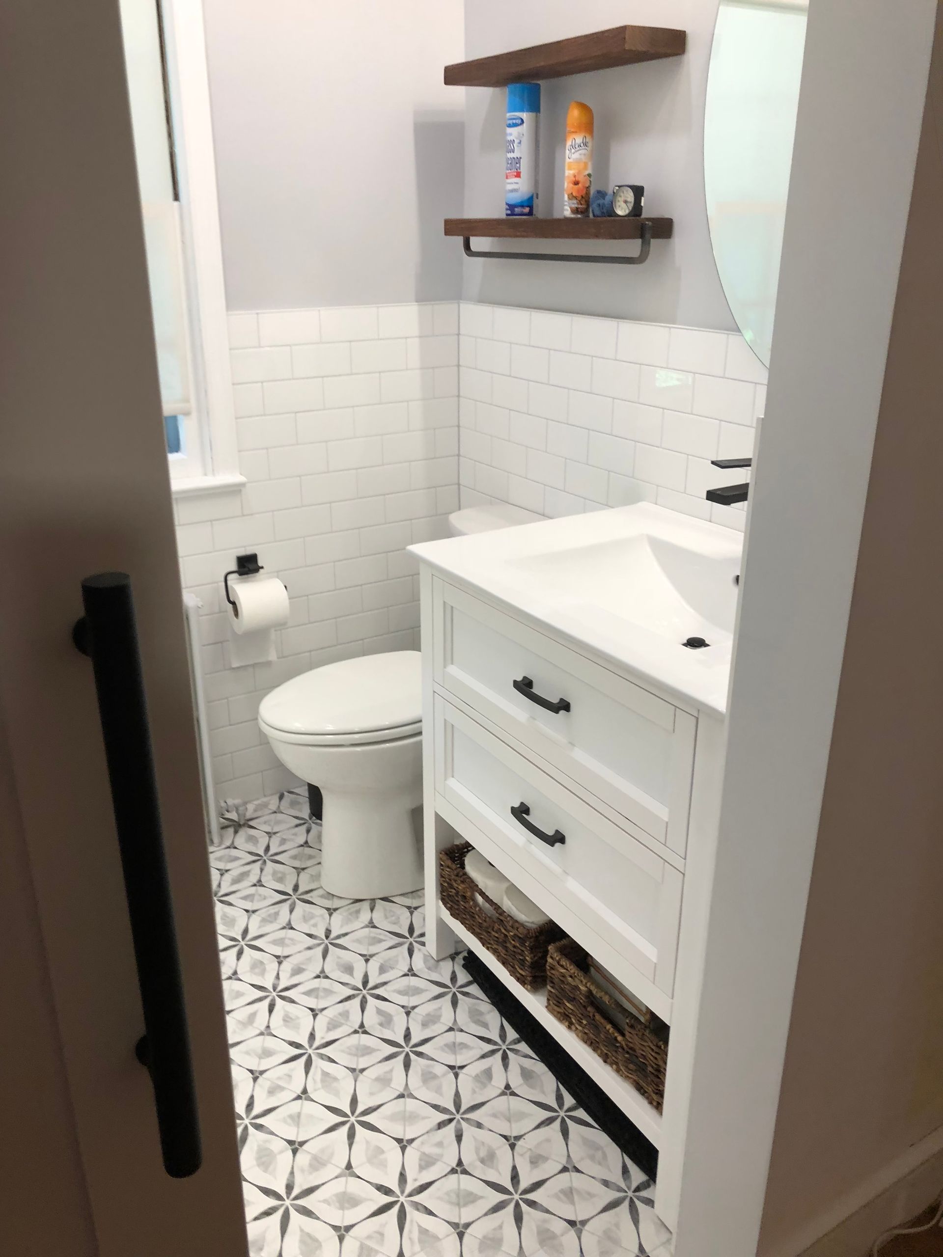 Small bathroom with white vanity, patterned floor, and white tile.
