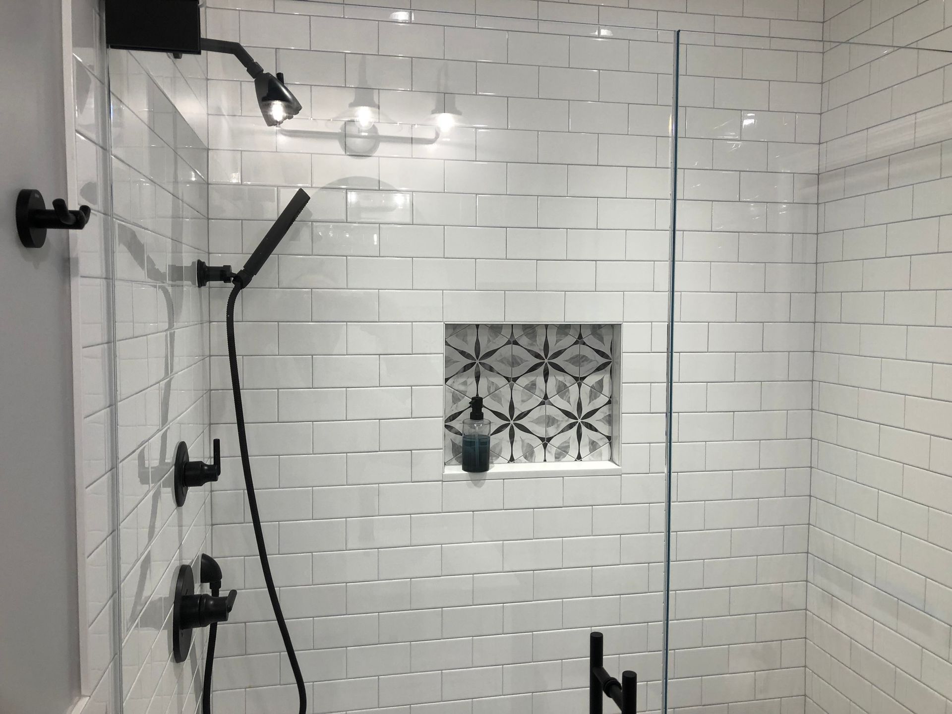 White tiled shower with black fixtures and a decorative tile niche.
