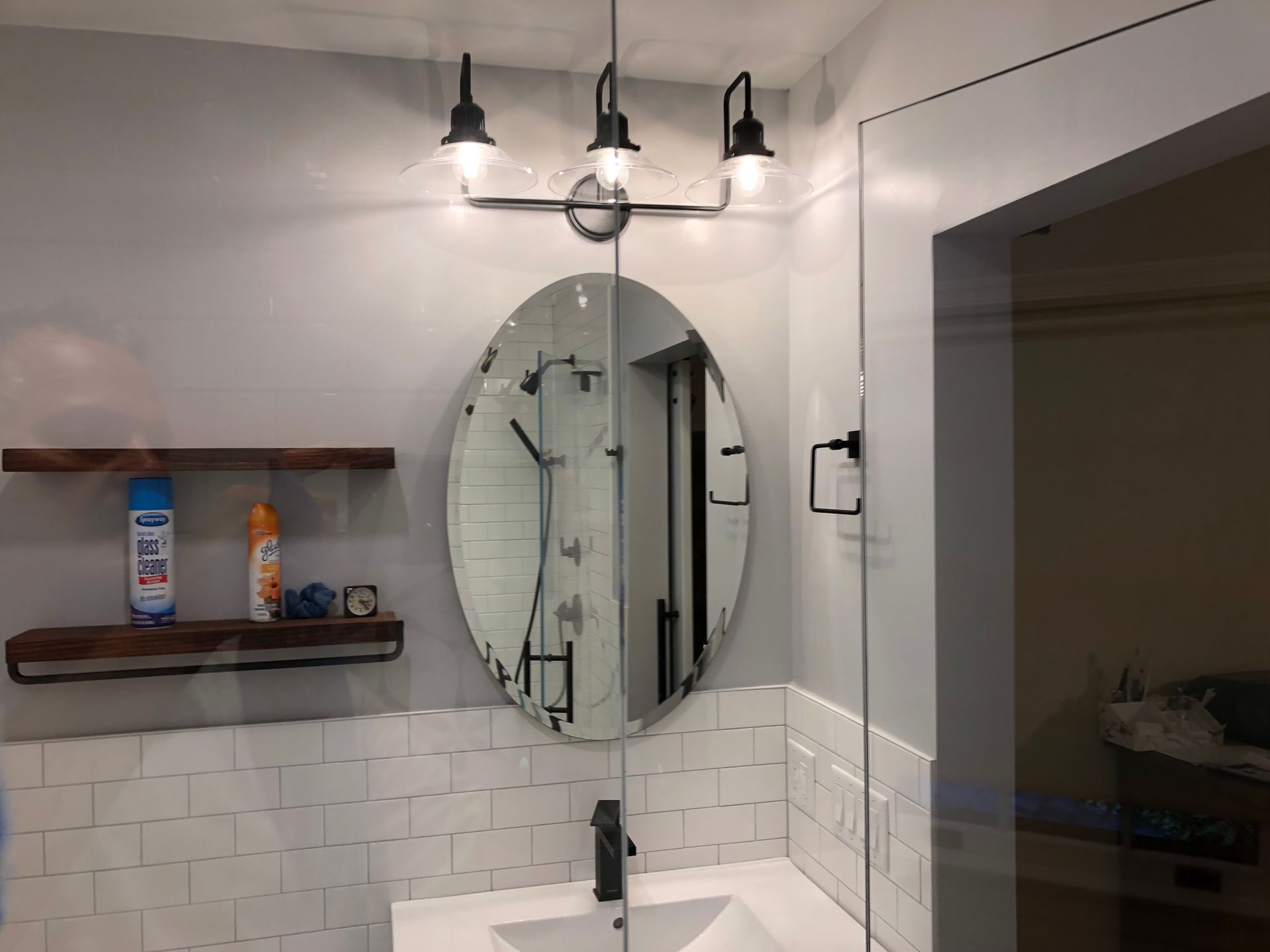 Bathroom with an oval mirror, overhead lights, and white subway tile. A shower is visible.