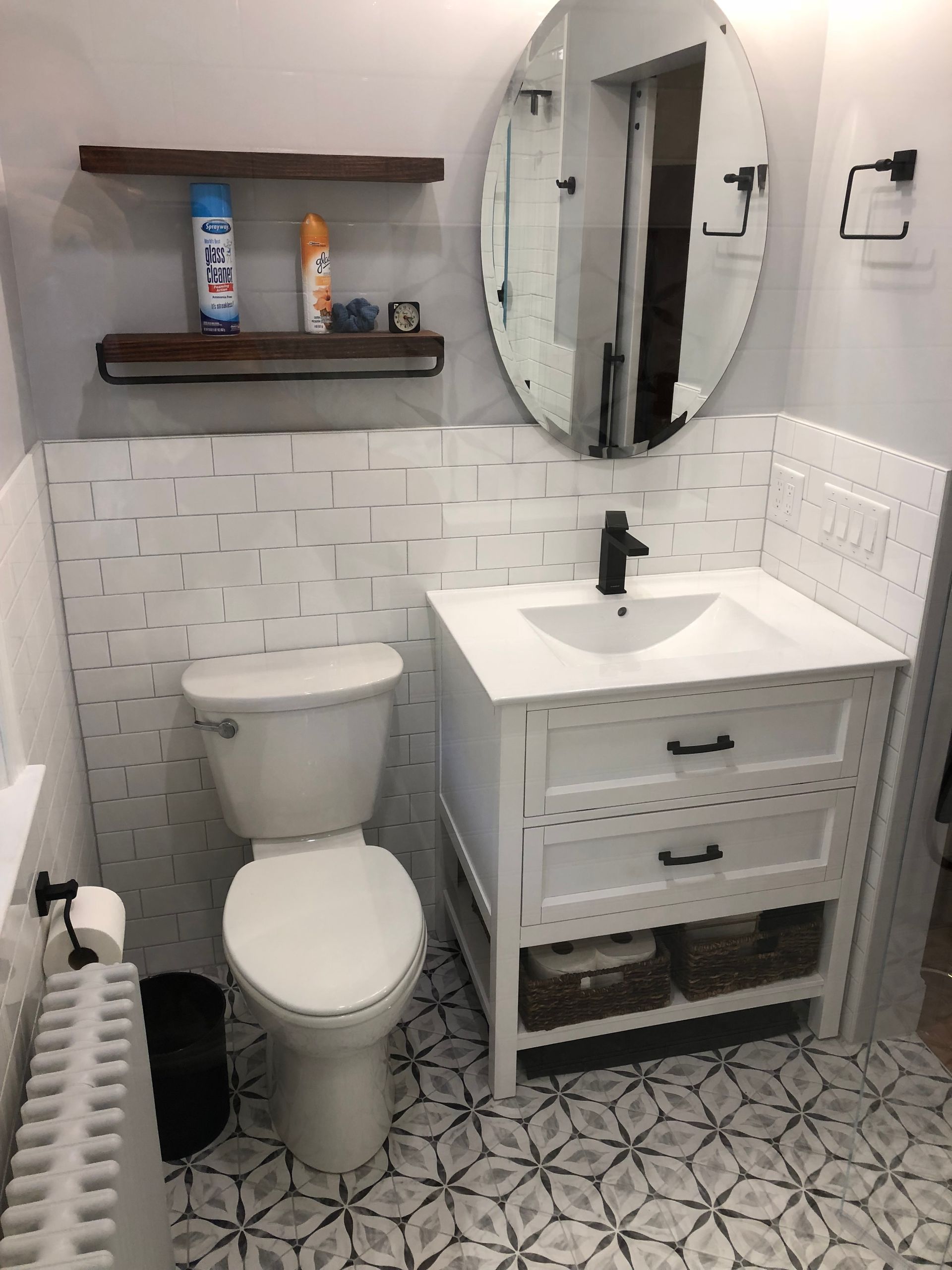 Bathroom with white vanity, toilet, oval mirror, and patterned floor tile.