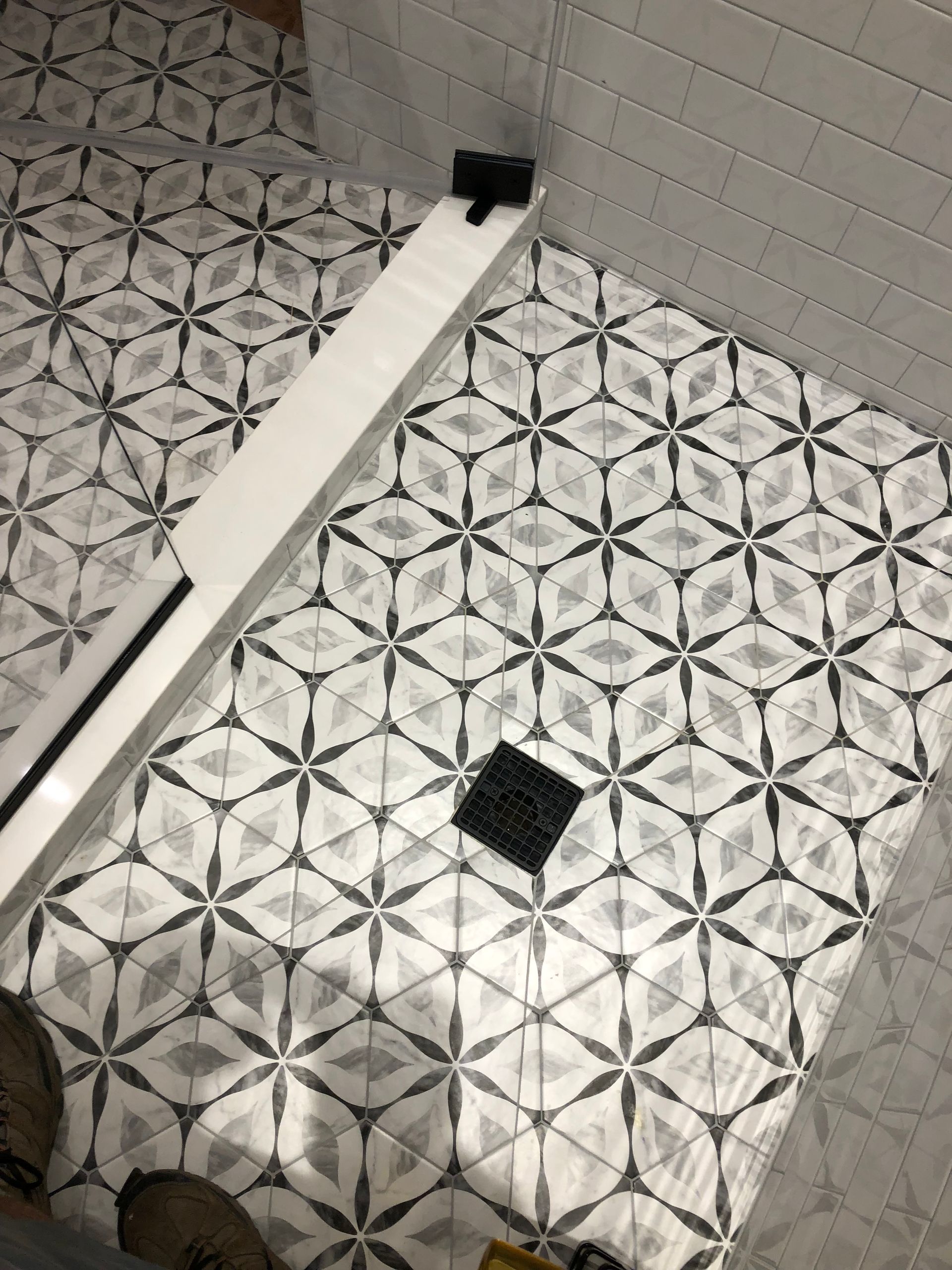 Bathroom floor with patterned tiles, drain, and shower edge.