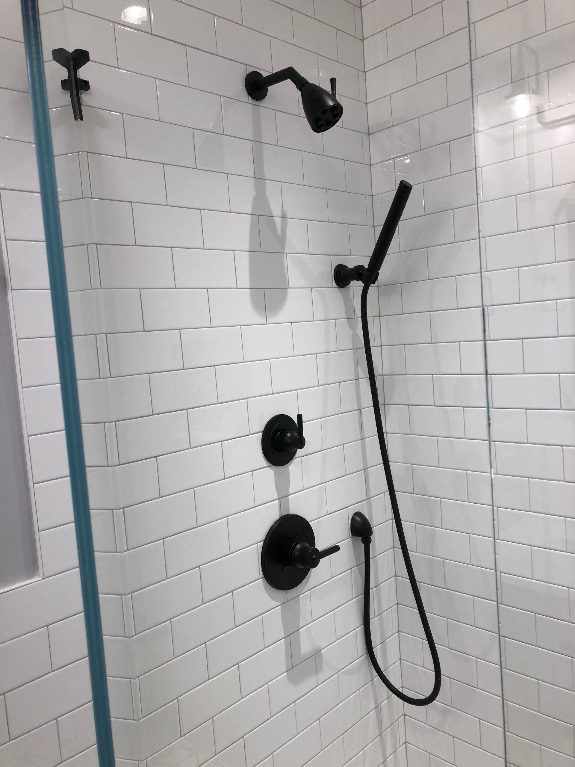 Black shower fixtures against white subway tile in a glass-enclosed shower.