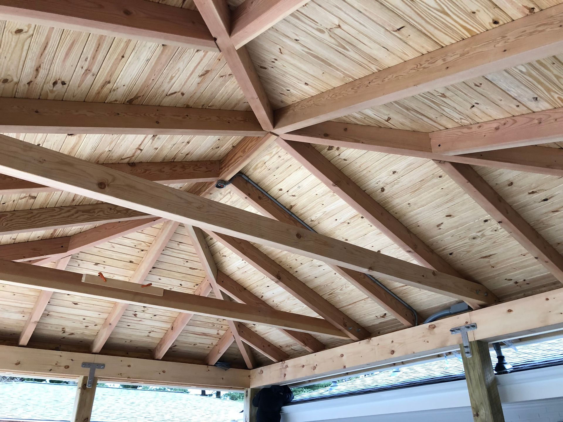 Wooden gazebo ceiling with exposed beams and light-colored panels.