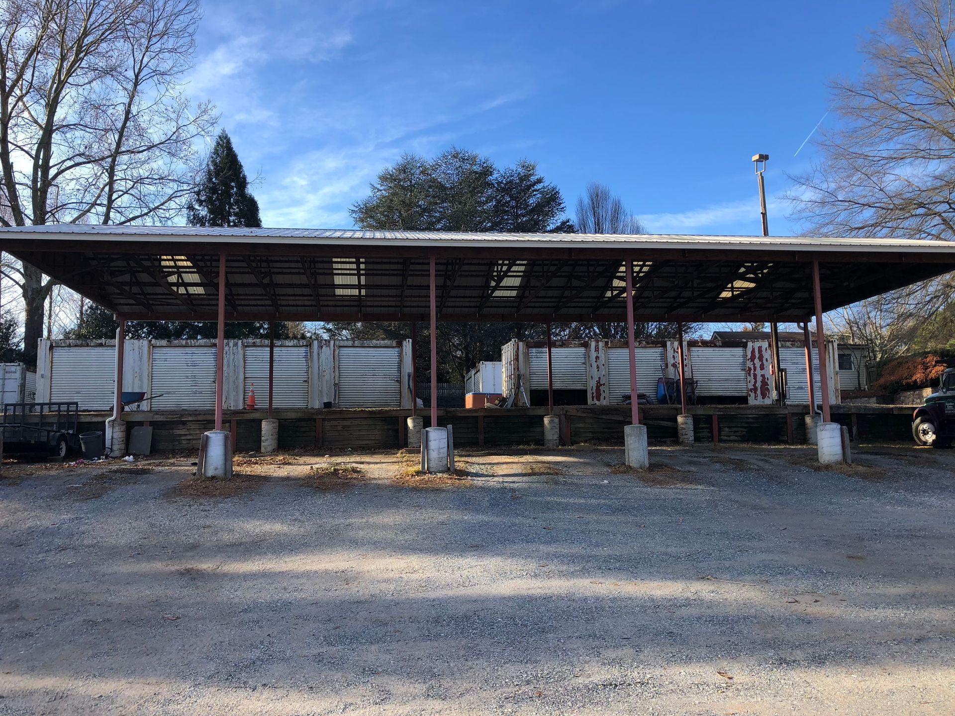 Covered recycling bins under a metal roof, outdoors.