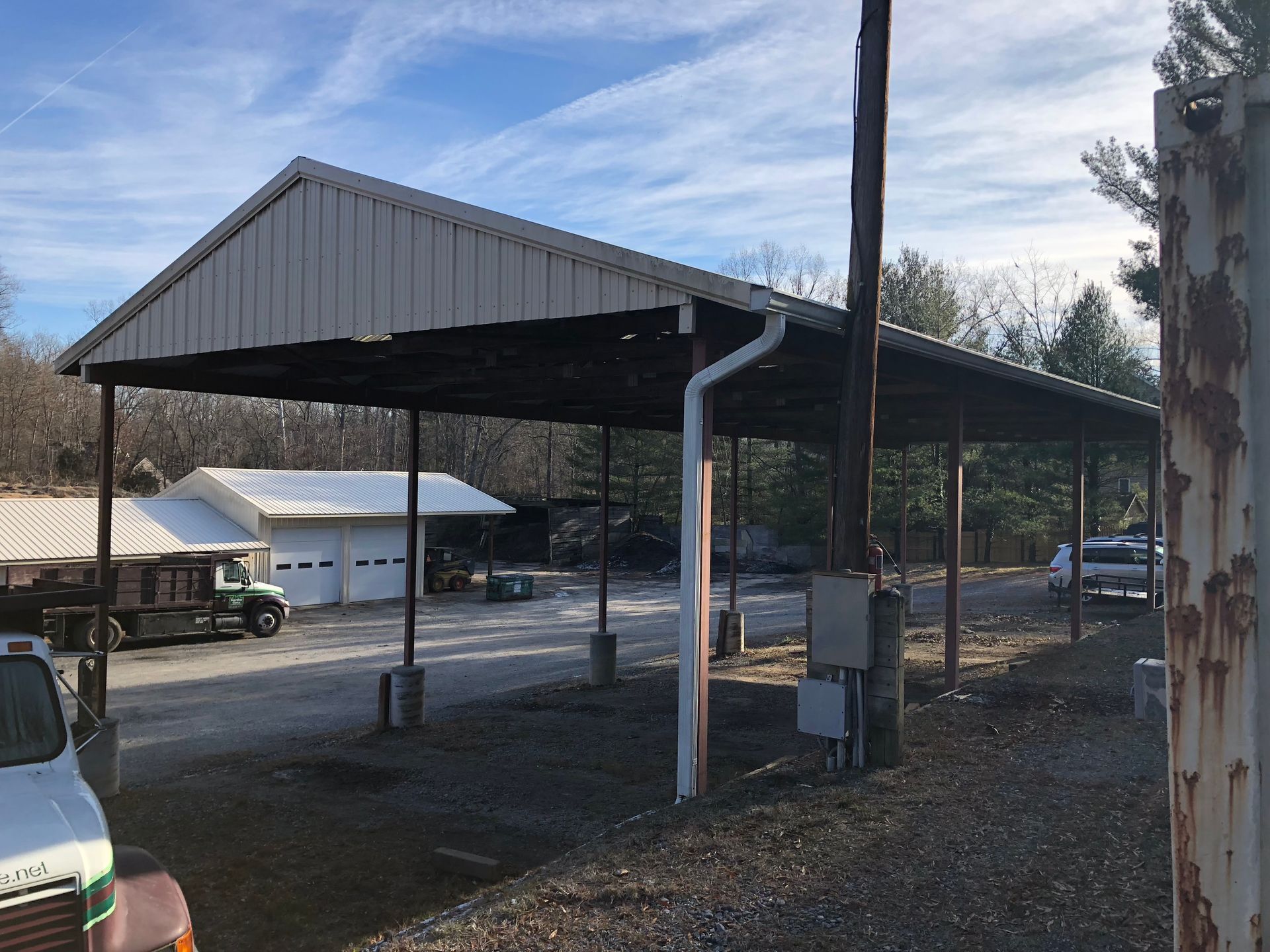 Metal carport over a gravel area, with a white building in the background.