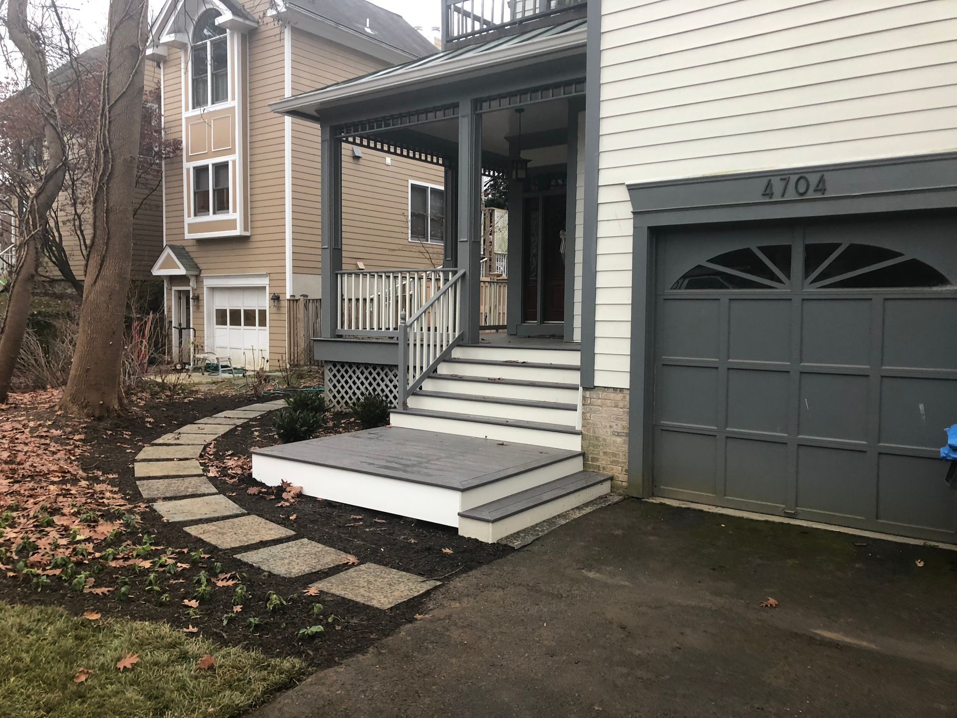 House with porch and steps, dark gray garage door, and stone path.