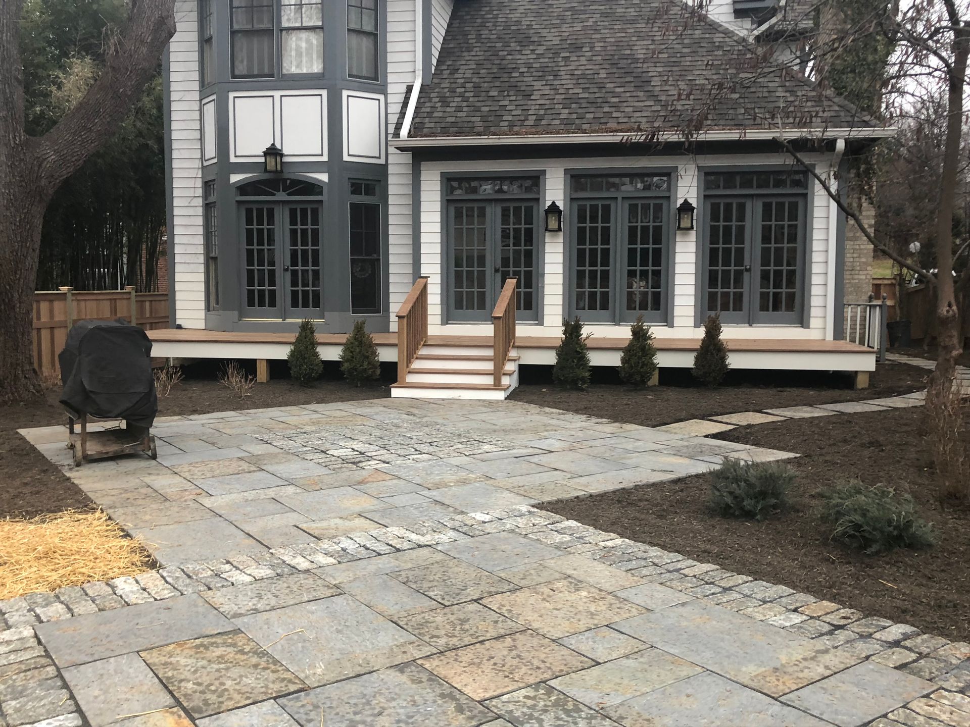 Stone patio leading to a multi-story house with a wooden deck and several windows.