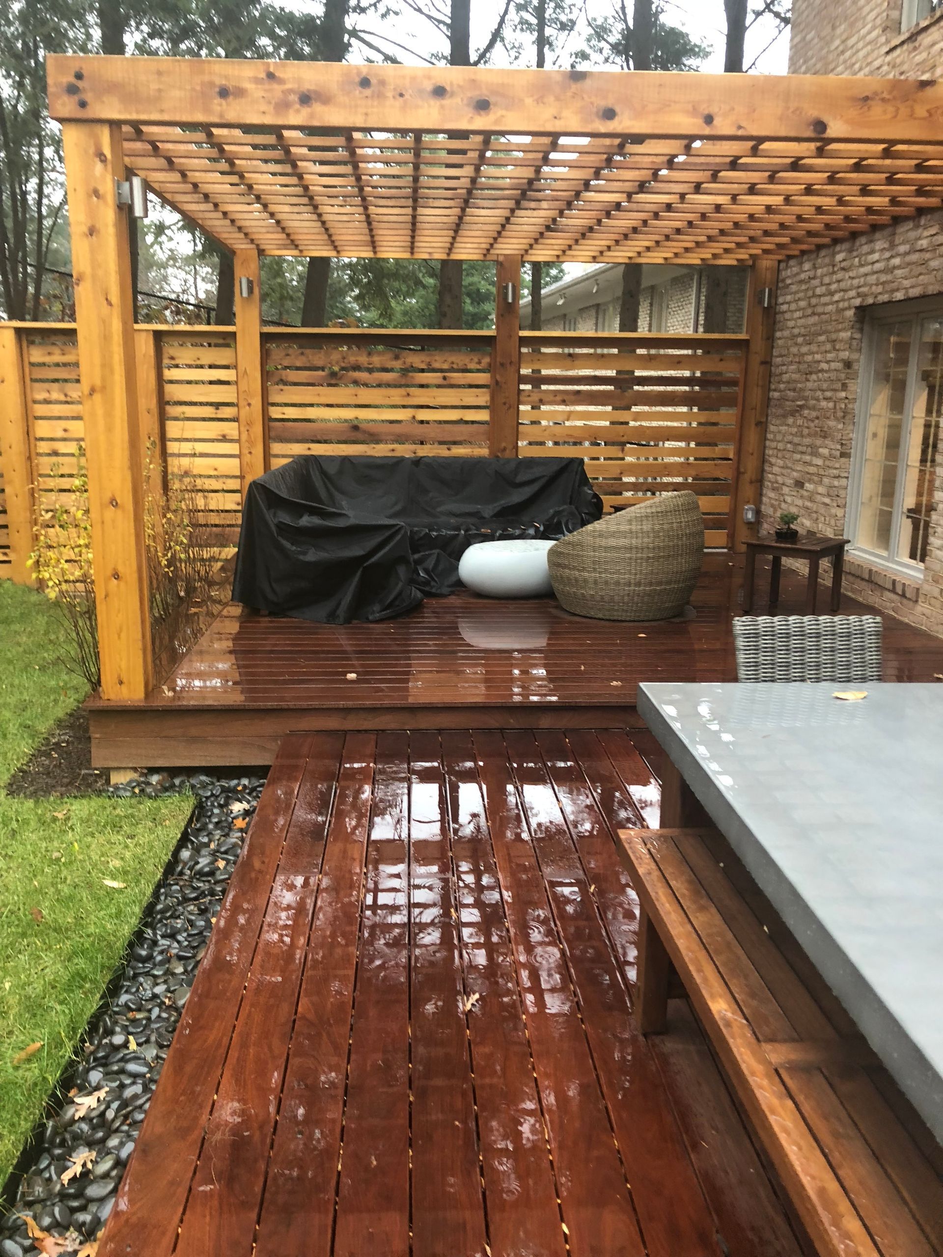 Wooden outdoor patio with a pergola, furniture, and wet wood in the rain.