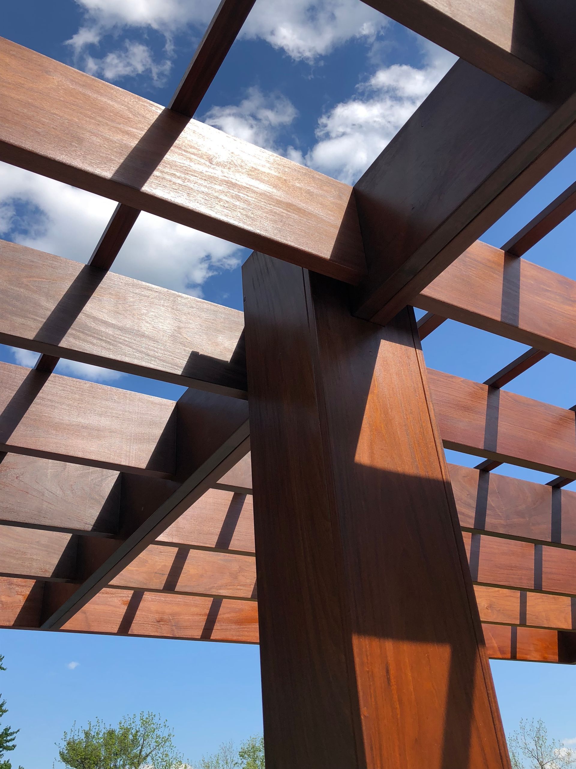 Wooden pergola with a grid roof against a blue sky with clouds.