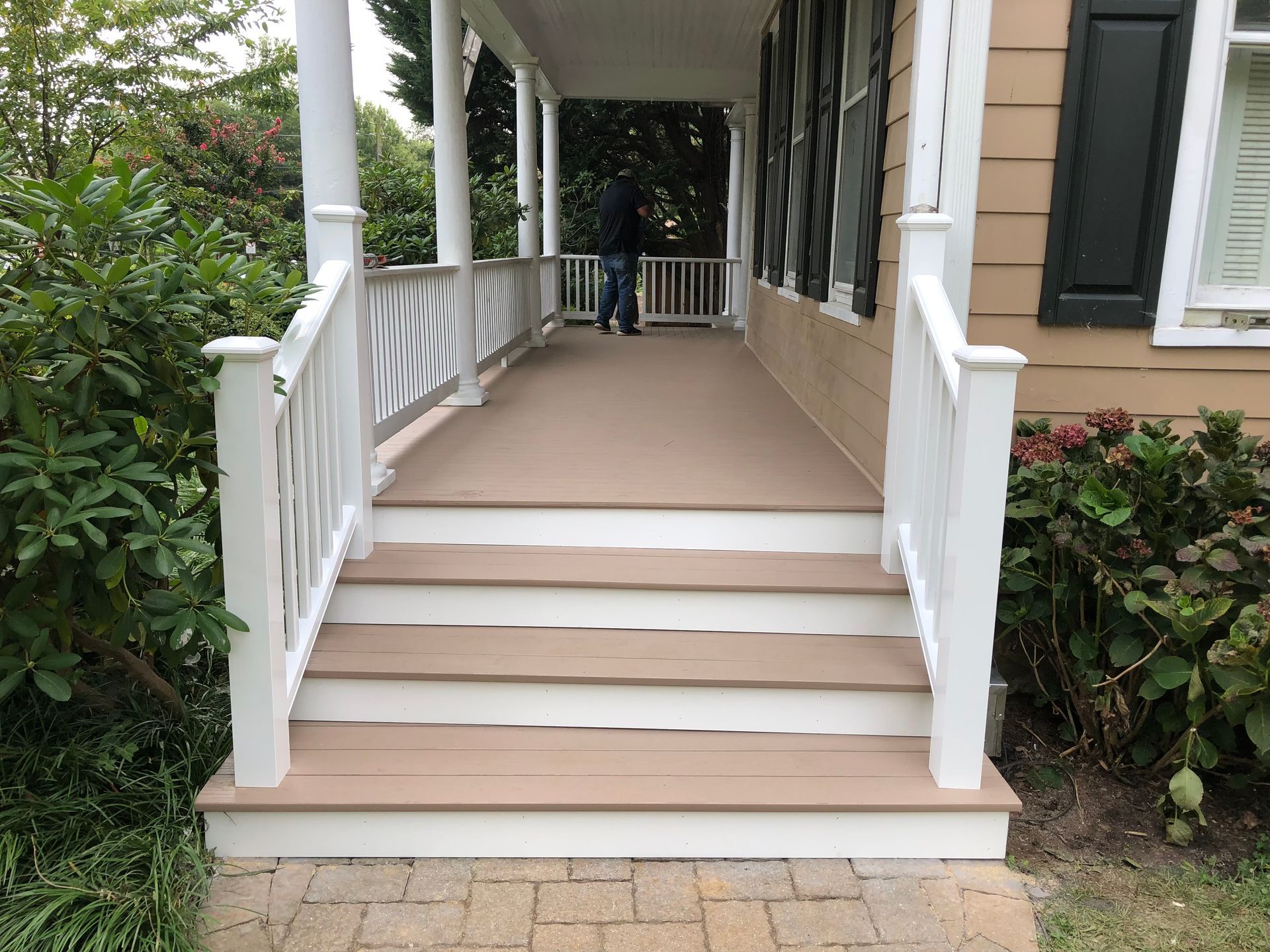 A white-railed porch with stairs. A person stands on the porch. The steps are light brown.