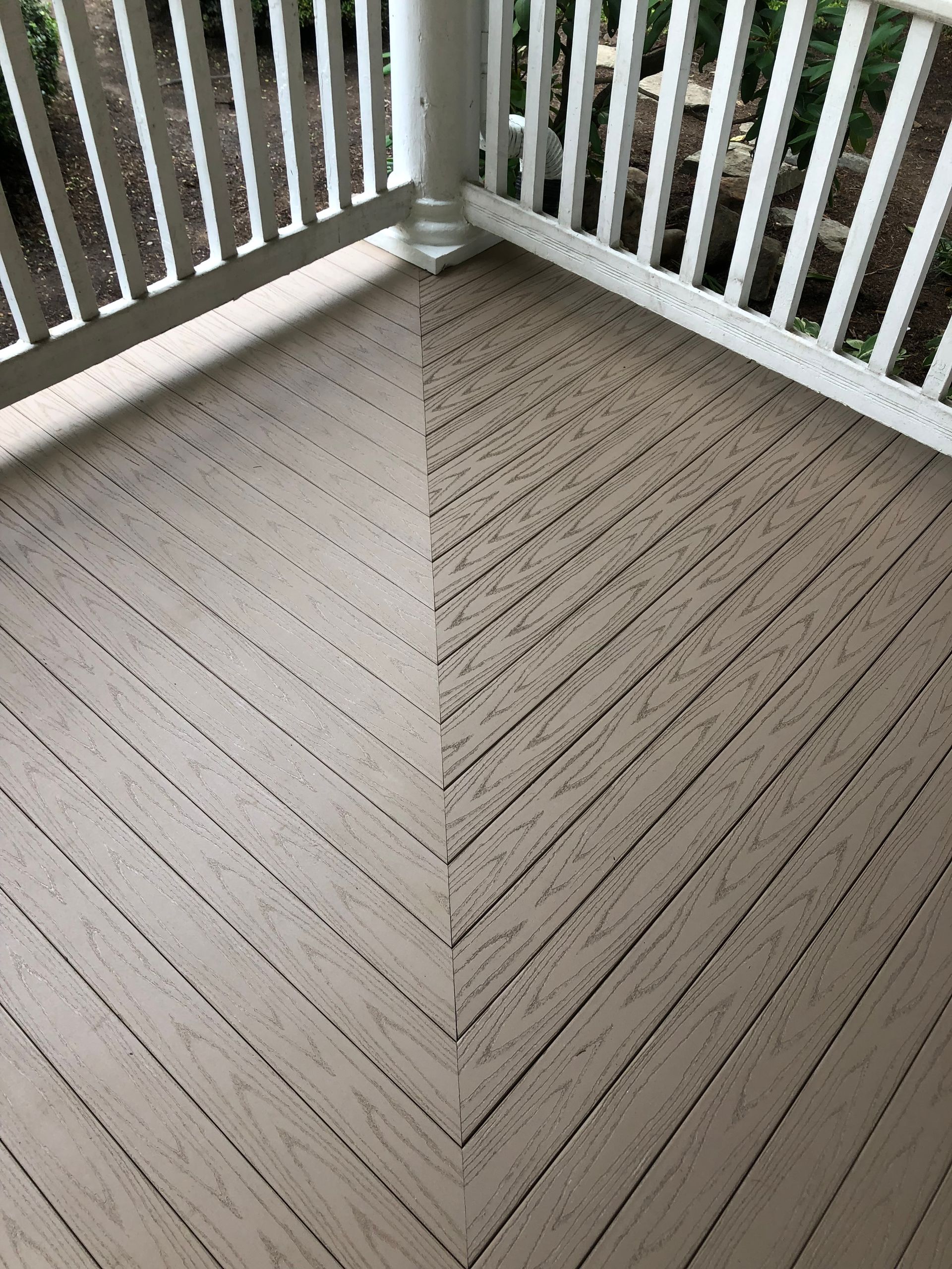 Angled, light-brown deck boards meet at a point. White railing and post in corner.
