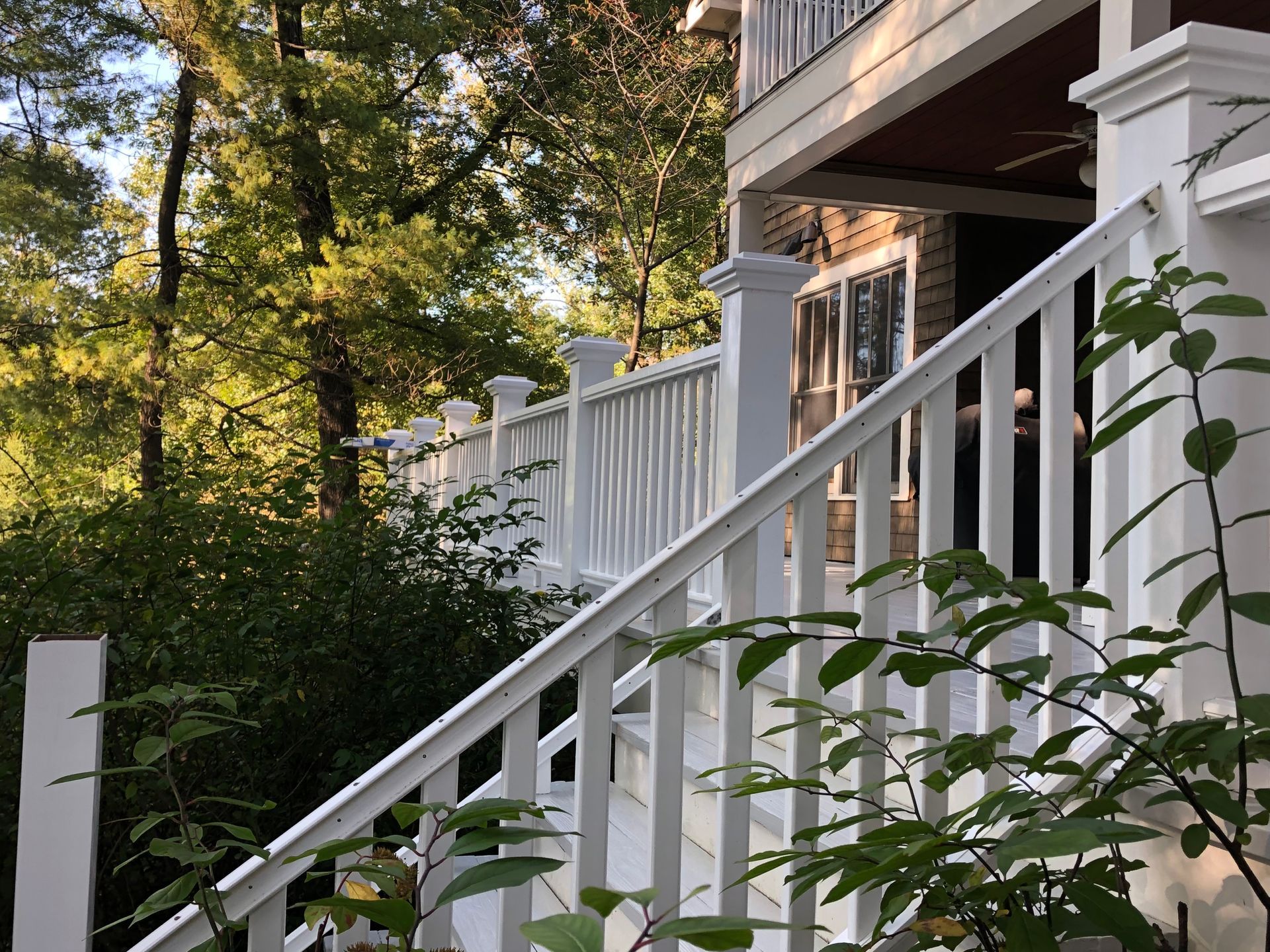 White wooden deck railing and stairs, with a building in the background surrounded by greenery.