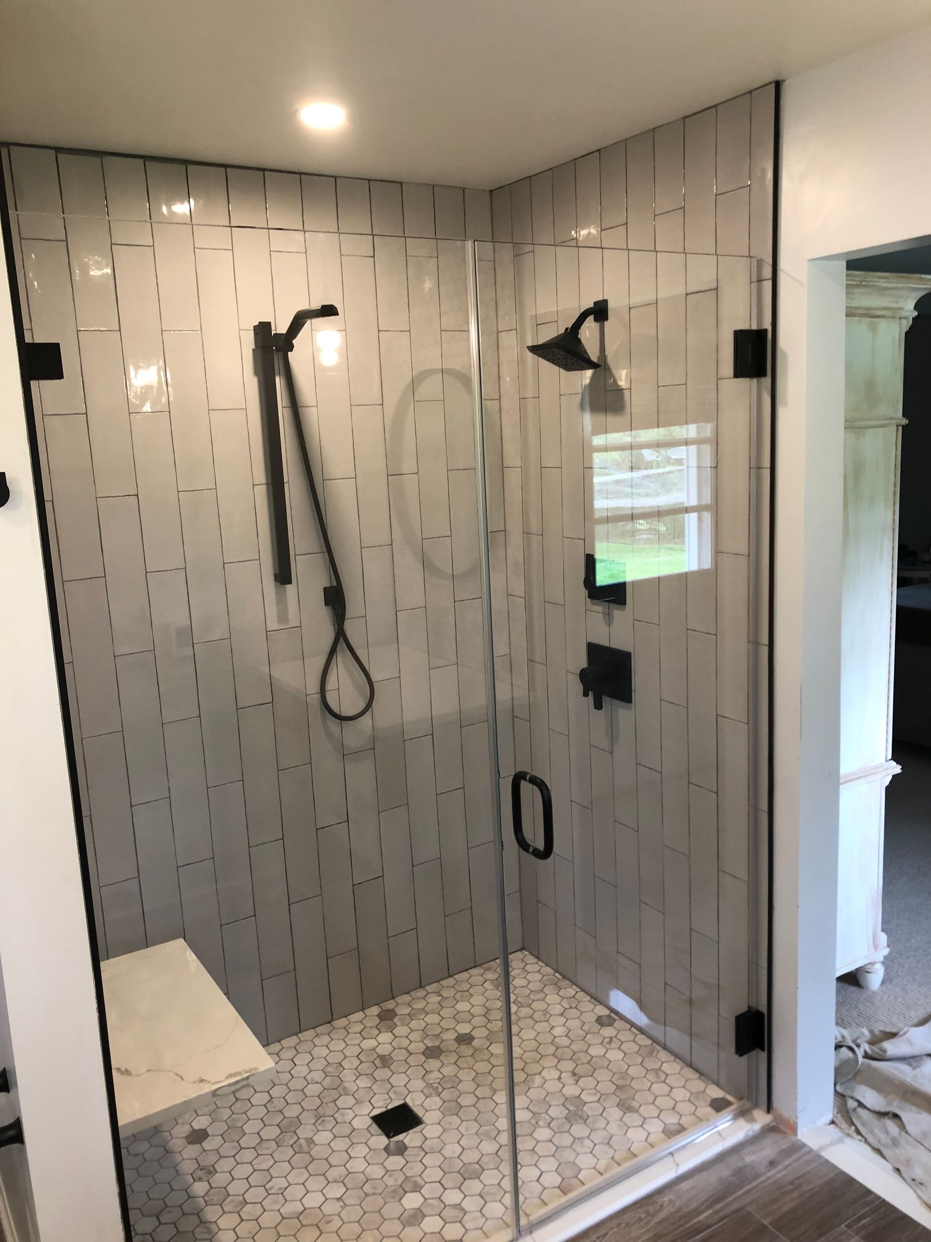 Glass shower with black fixtures and white rectangular tiled walls; pebble stone floor.
