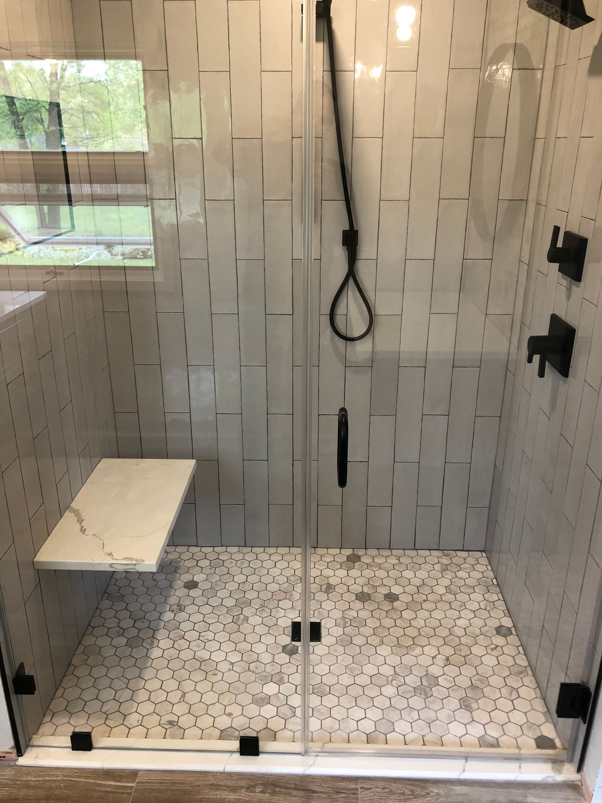 Modern tiled shower with glass doors, a built-in seat, and black fixtures.