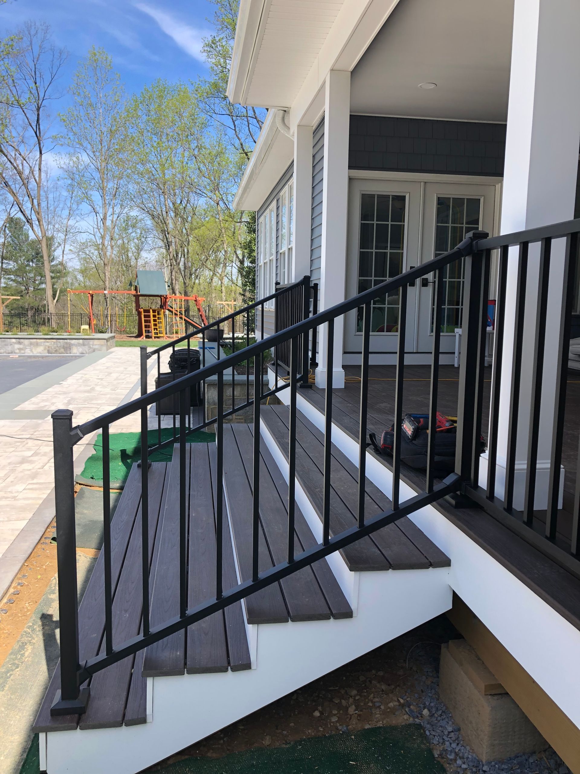 Black railing and steps leading up to a porch with white trim and a playground visible in the background.