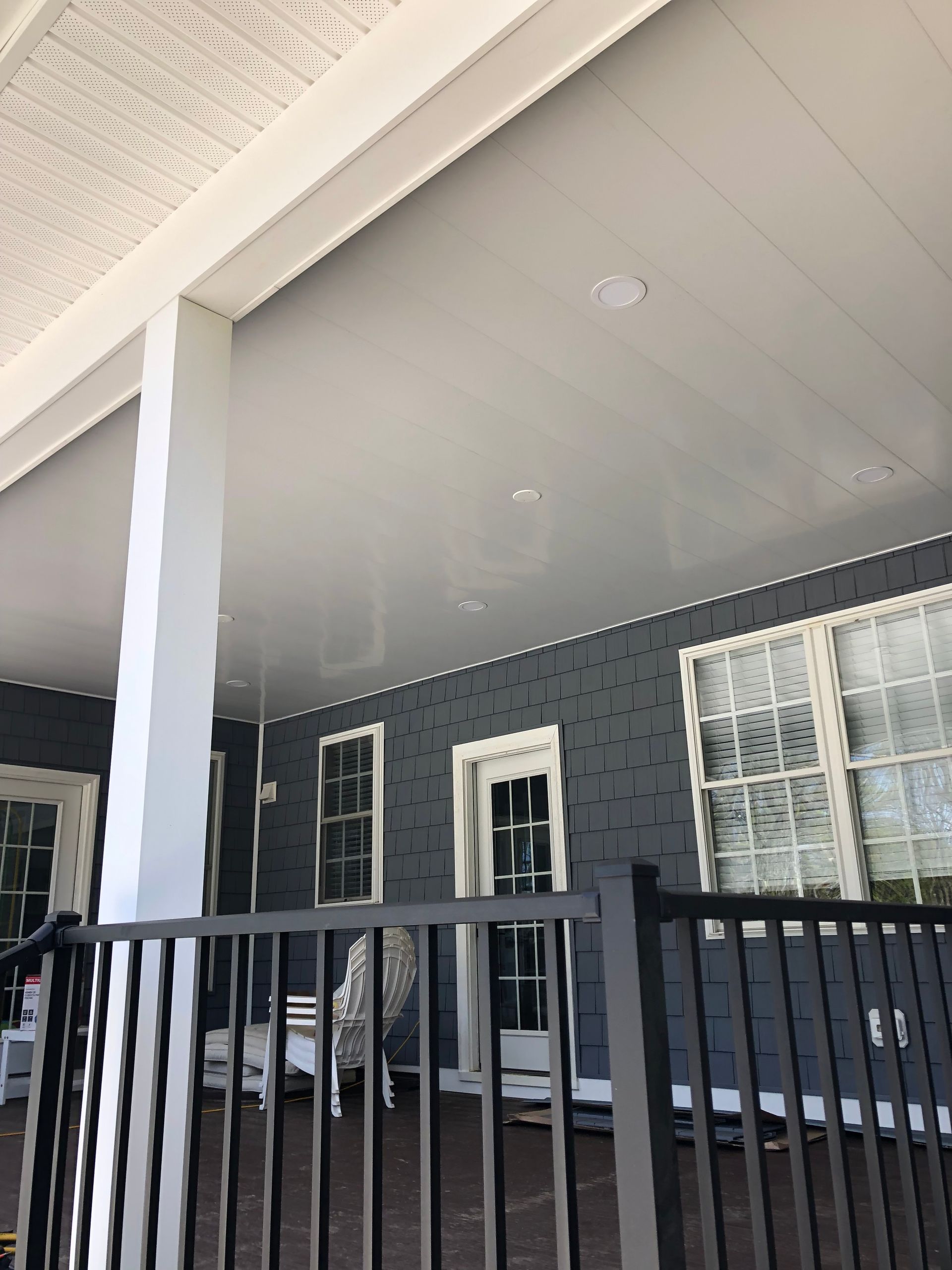 Covered porch with white ceiling and support column, dark gray siding, and black fence.